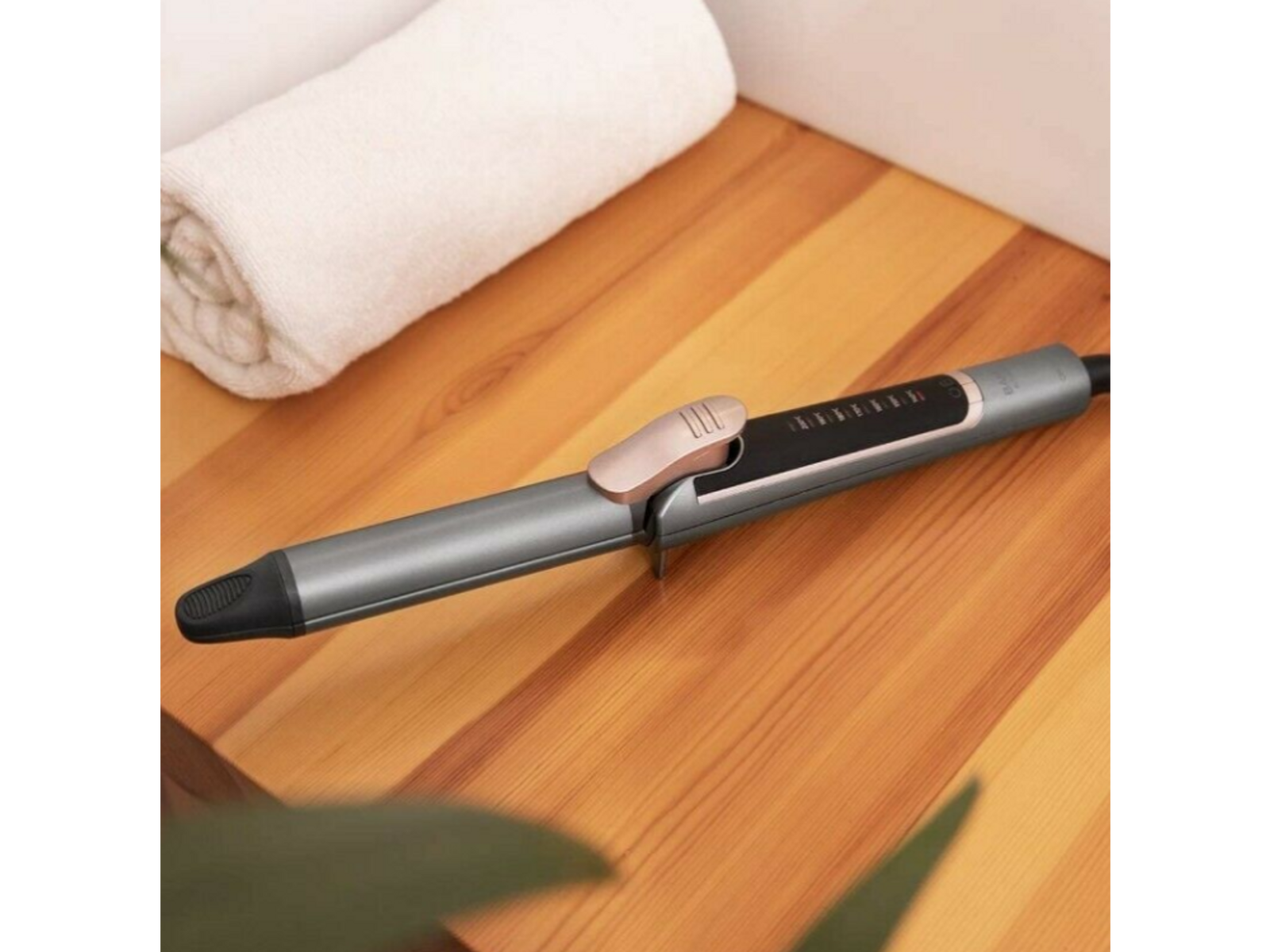 Rizador de pelo sobre superficie de madera con toalla blanca al fondo.