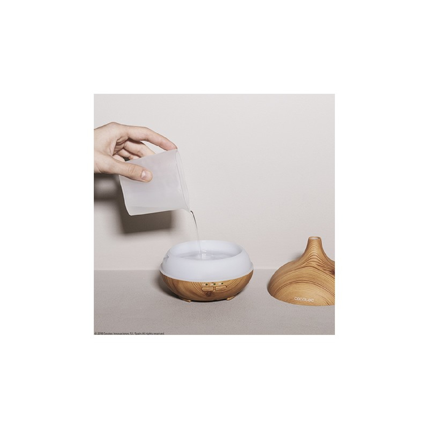 Una mano versa acqua in un diffusore in legno. Il diffusore e il coperchio sono su una superficie neutra.