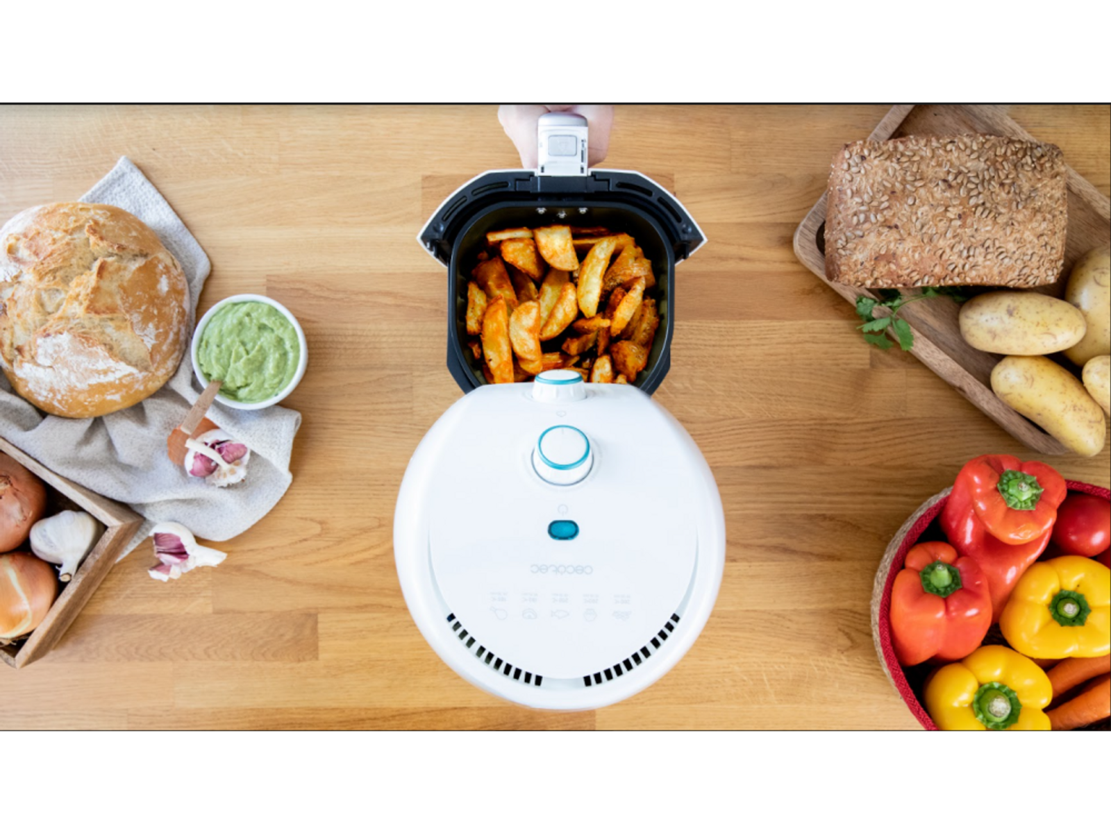 Vista superior de una freidora de aire con patatas cocinadas, rodeada de alimentos.