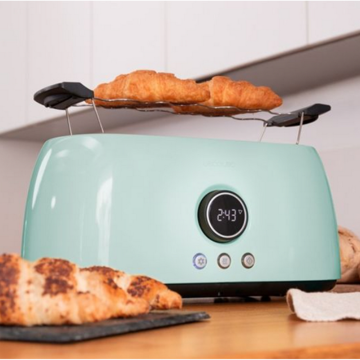 Tostapane verde acqua con due croissant sopra e uno sotto, tavolo di legno.