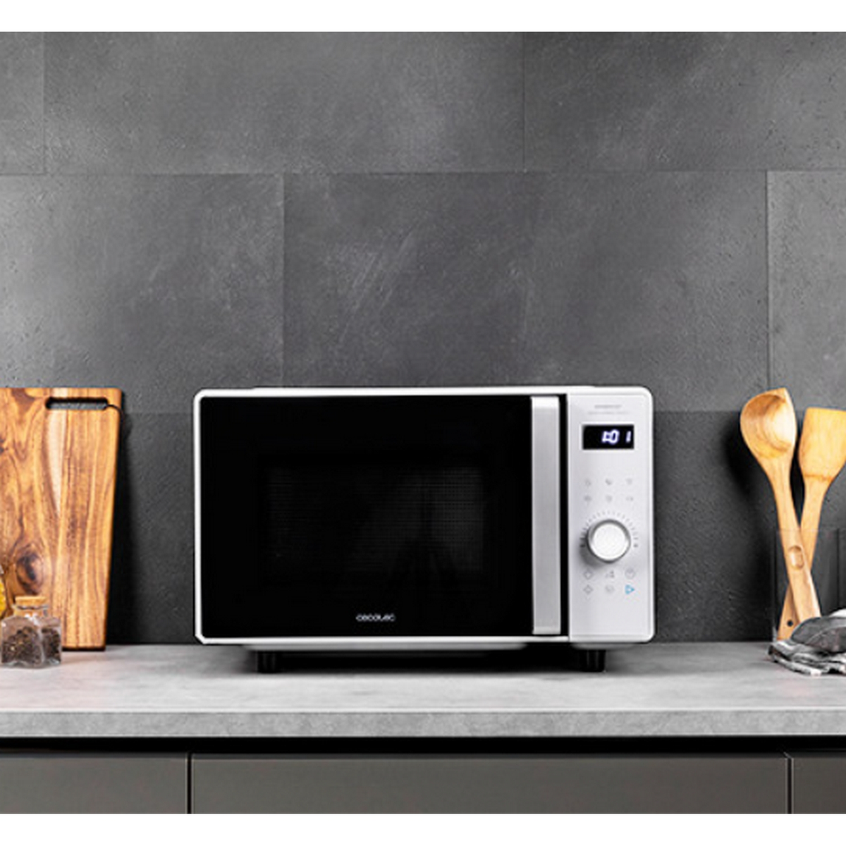 Biała kuchenka mikrofalowa z wyświetlaczem cyfrowym i panelem sterowania na szarym blacie z przedmiotami.