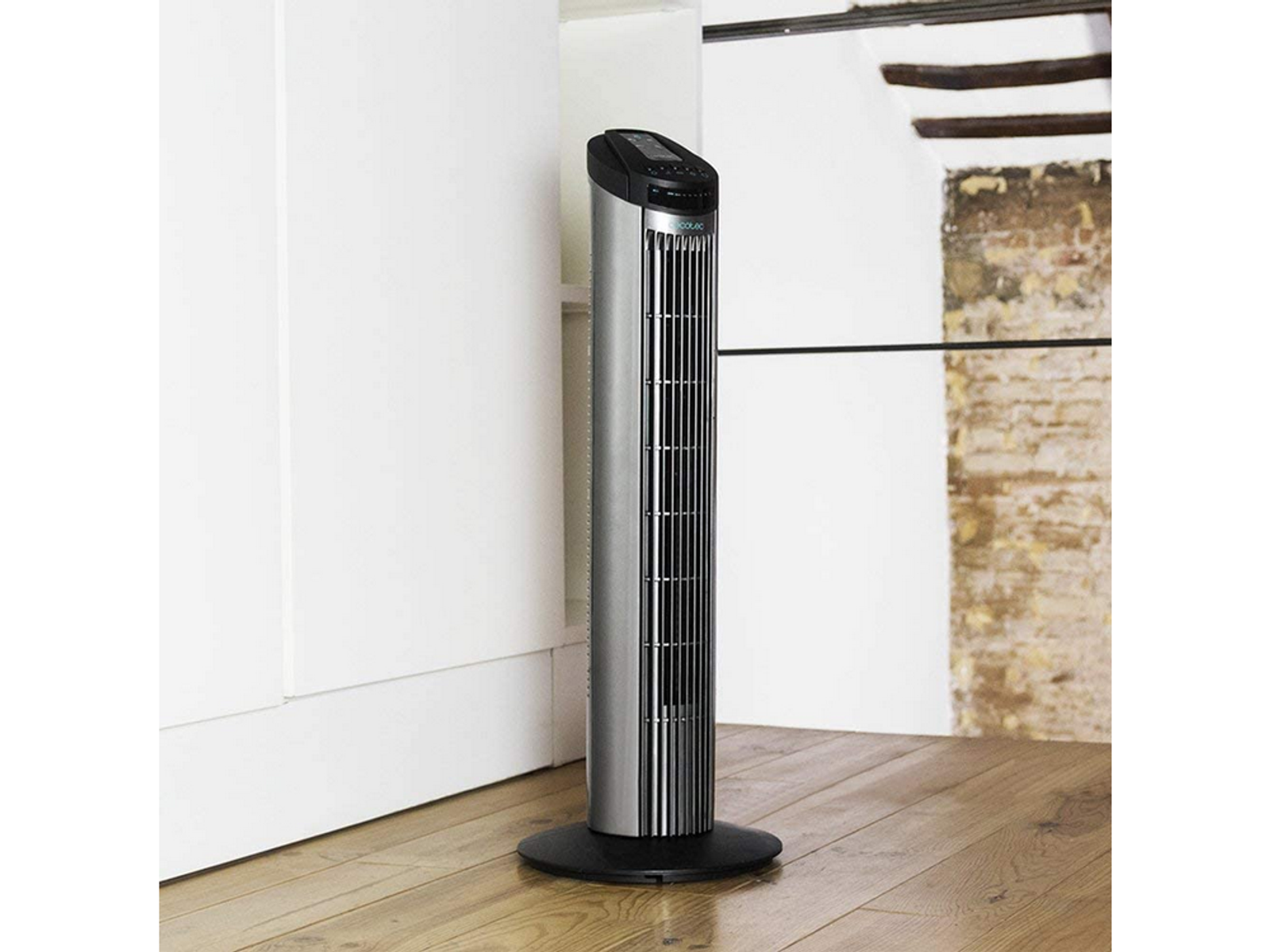 Wysoki, srebrny wentylator stojący na czarnej podstawie, w pokoju z drewnianą podłogą.