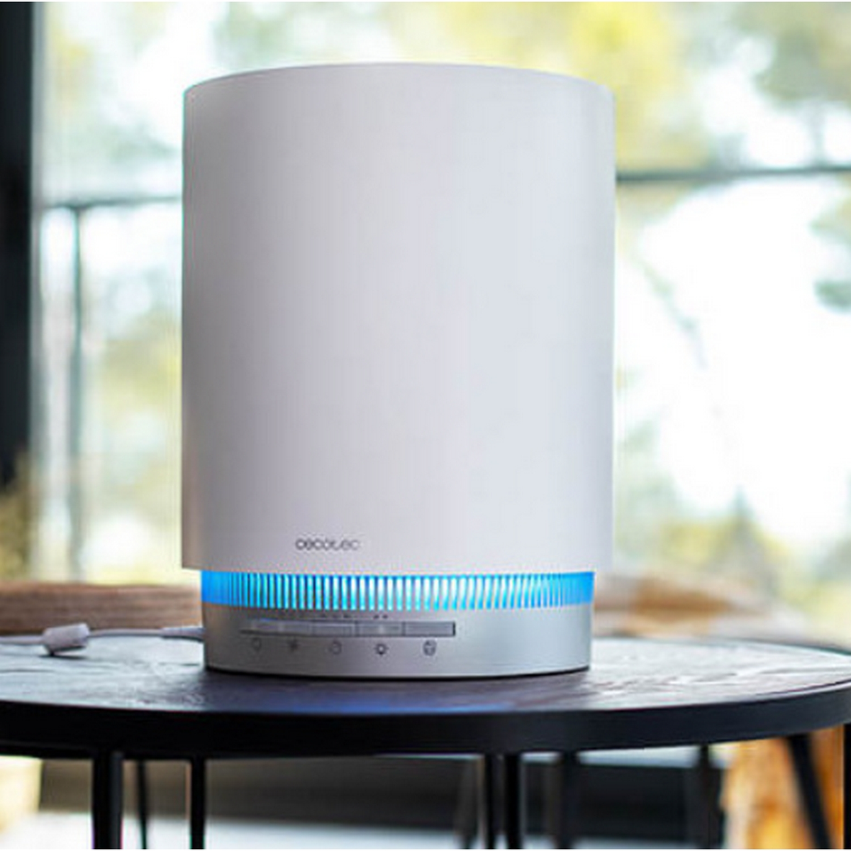 Un umidificatore bianco con luci blu. Si trova su un tavolo scuro. Ha una base e dei comandi argentati.