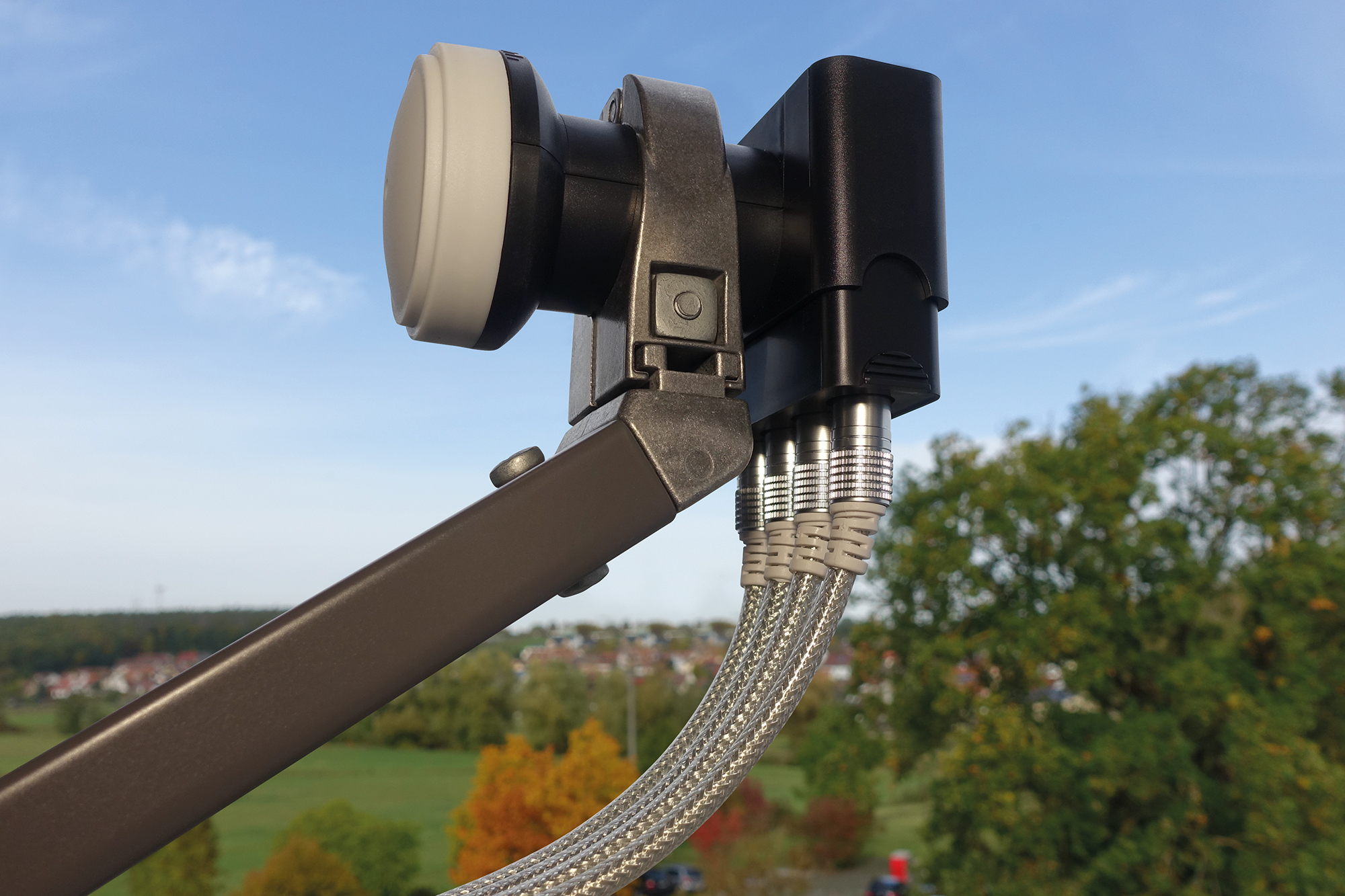 Element anteny satelitarnej, czarny i srebrny, na tle błękitnego nieba i zielonych drzew.