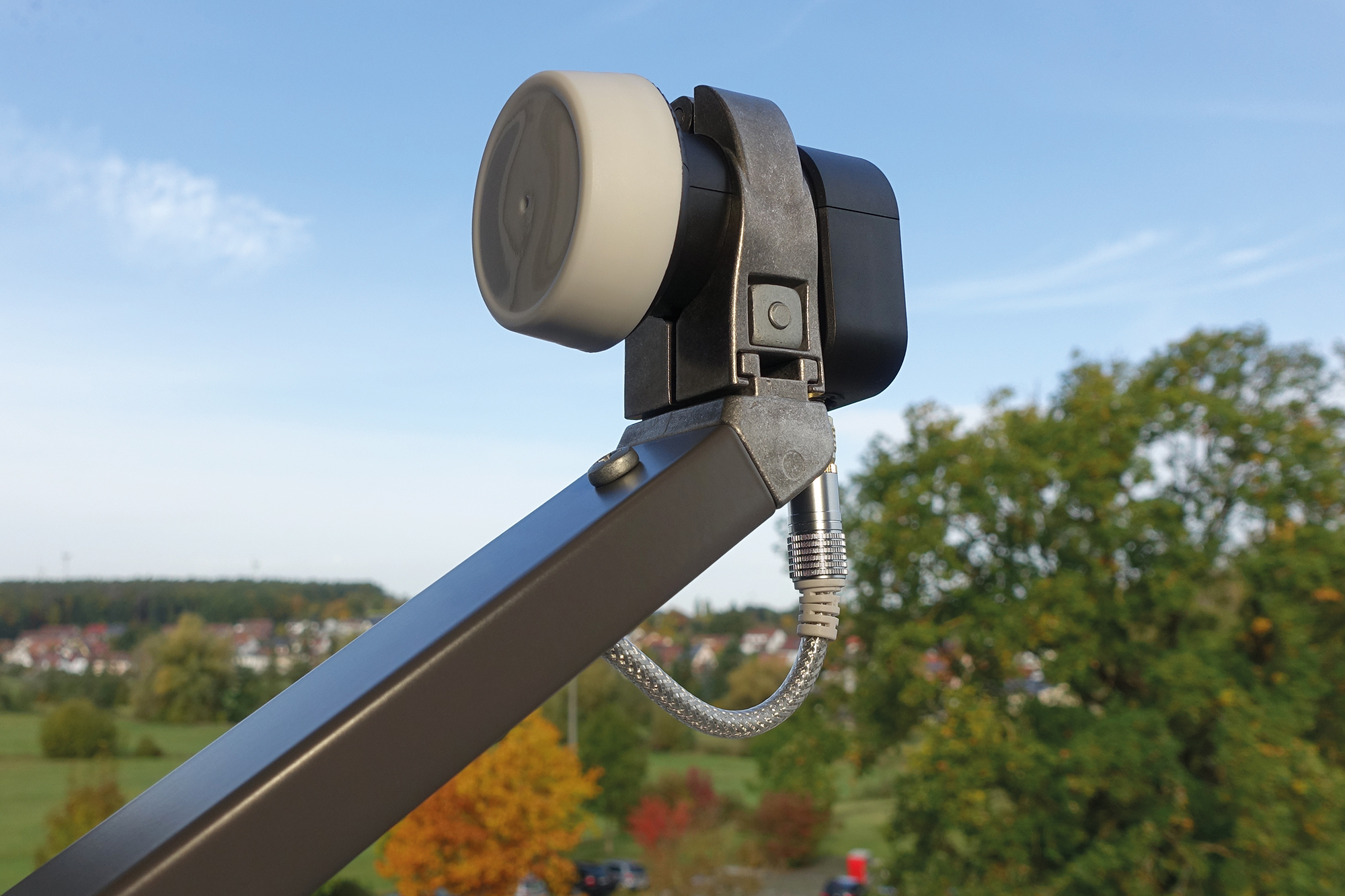 Antena satelitarna z czarnym ramieniem, zamontowana na zewnątrz. Błękitne niebo i drzewa w tle.