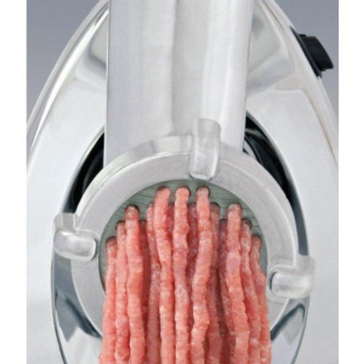 Zbliżenie maszynki do mielenia mięsa wytłaczającej przetworzone mięso. Widoczna jest maszynka i mięso.