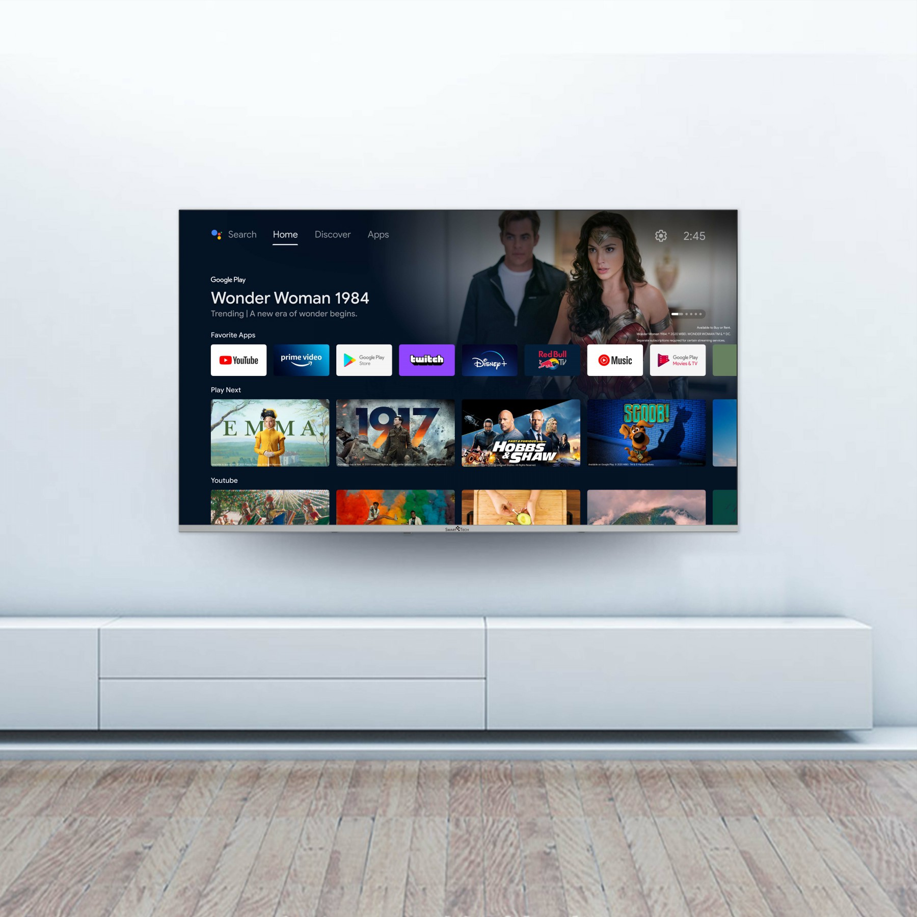 Duży ekran telewizora wyświetlający interfejs Smart TV. Jest zamontowany na białej szafce na białej ścianie.