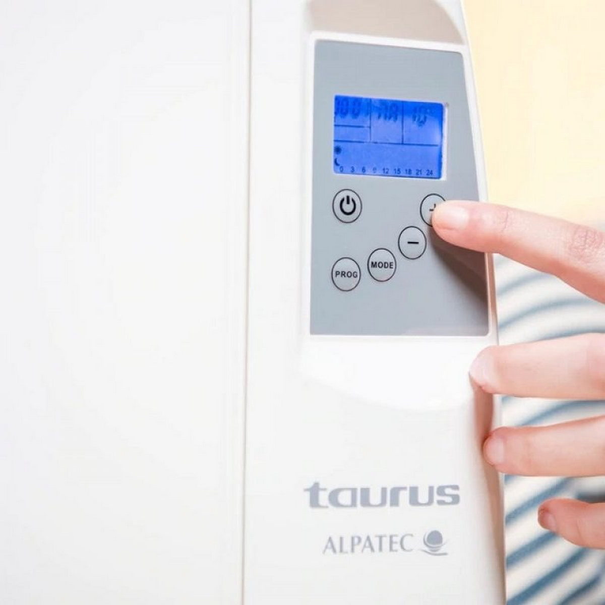 Eine Hand stellt einen digitalen Thermostat ein. Das Gerät ist weiß, mit blauem Display und der Marke Taurus.