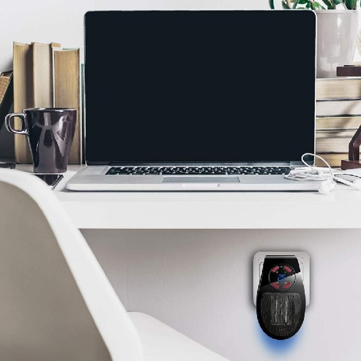 Un laptop, una tazza e un riscaldatore a spina sono su una scrivania con libri e una sedia.
