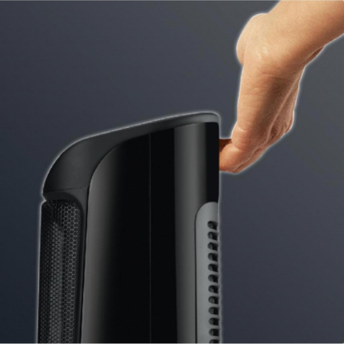 Ręka sięga po czarny, wysoki, cylindryczny grzejnik, chwytając uchwyt.