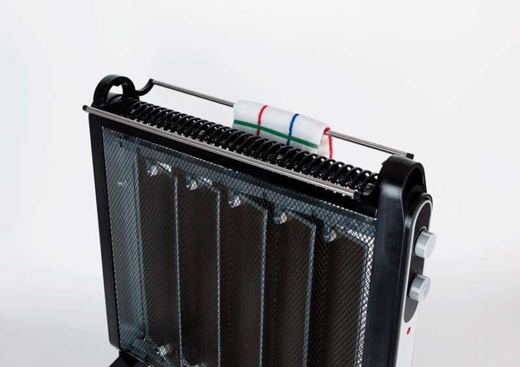 Radiador eléctrico negro y plateado con toalla secándose. Fondo blanco.