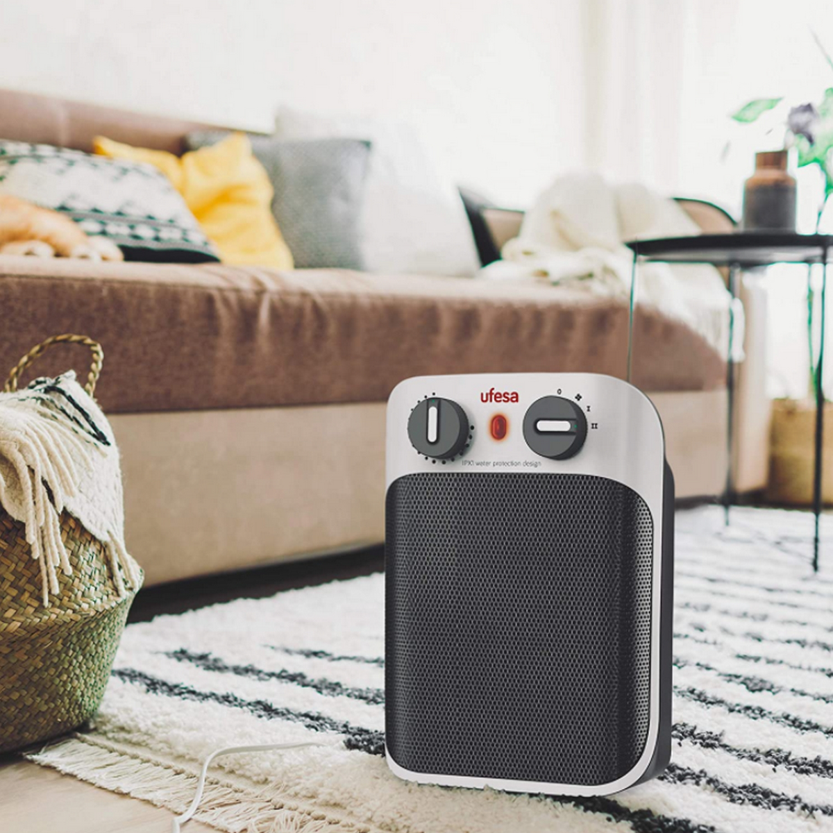 Czarno-biały grzejnik elektryczny z dwoma pokrętłami, umieszczony na dywanie przed sofą.