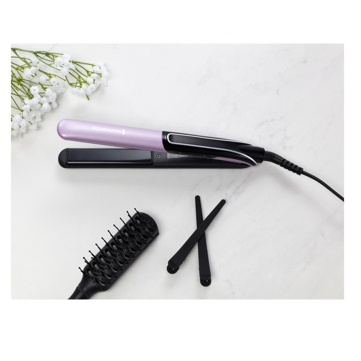 Piastra per capelli e accessori su una superficie bianca. Include una spazzola e delle clip, vista dall'alto.