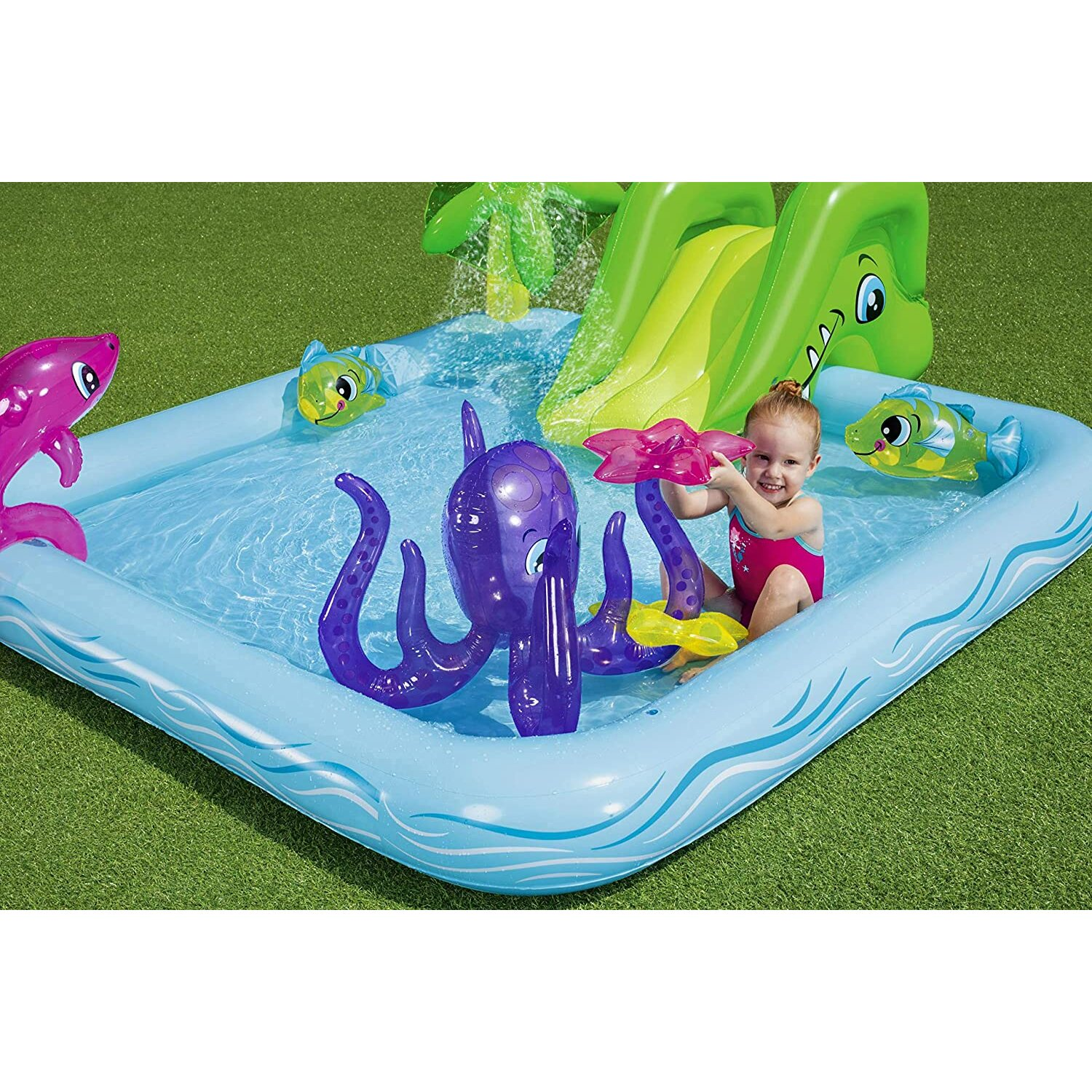 Ein Kind spielt in einem blauen aufblasbaren Pool mit Wasserrutsche und Spielzeug-Oktopus. Andere aufblasbare Spielzeuge sind vorhanden.