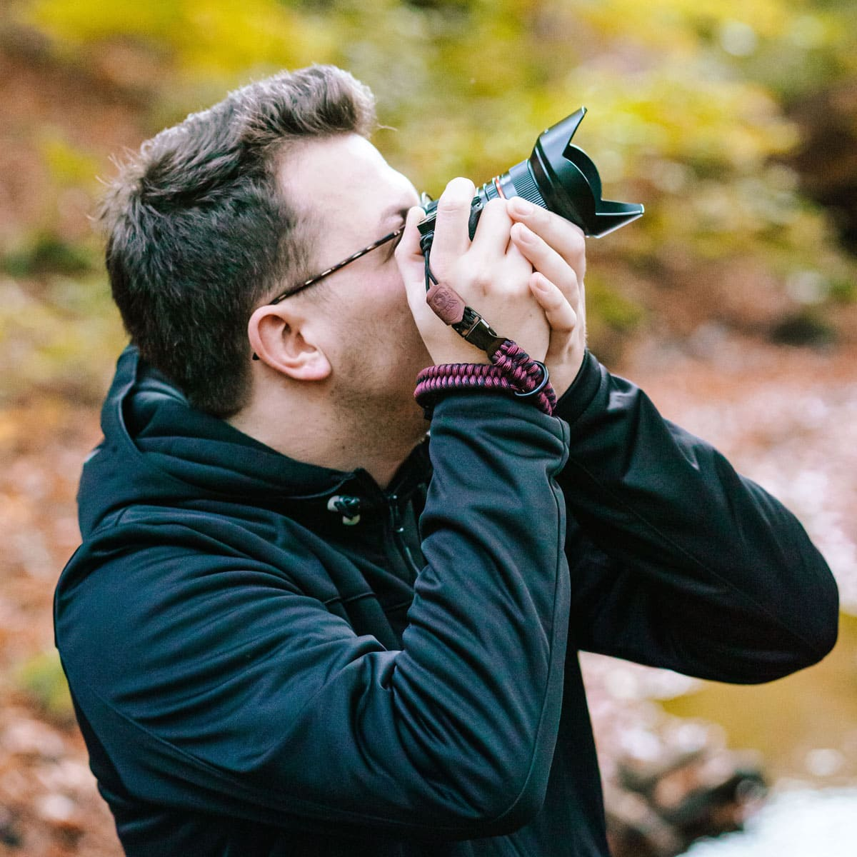 Mann fotografiert mit Kamera. Brille und Armband, unscharfer Hintergrund.