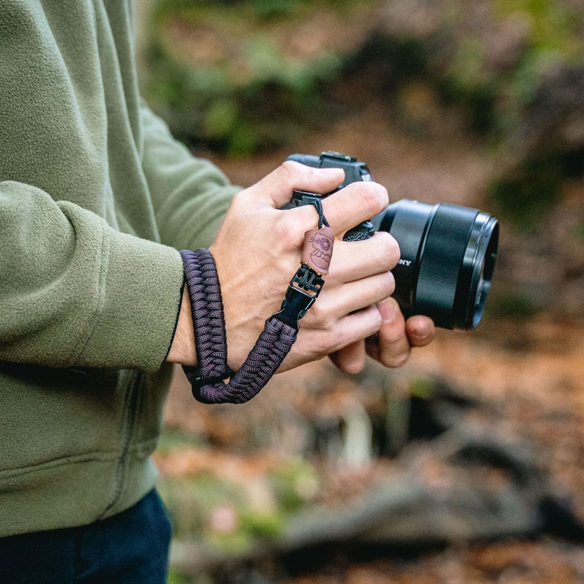 Persona che tiene una fotocamera con cinturino da polso in un bosco.
