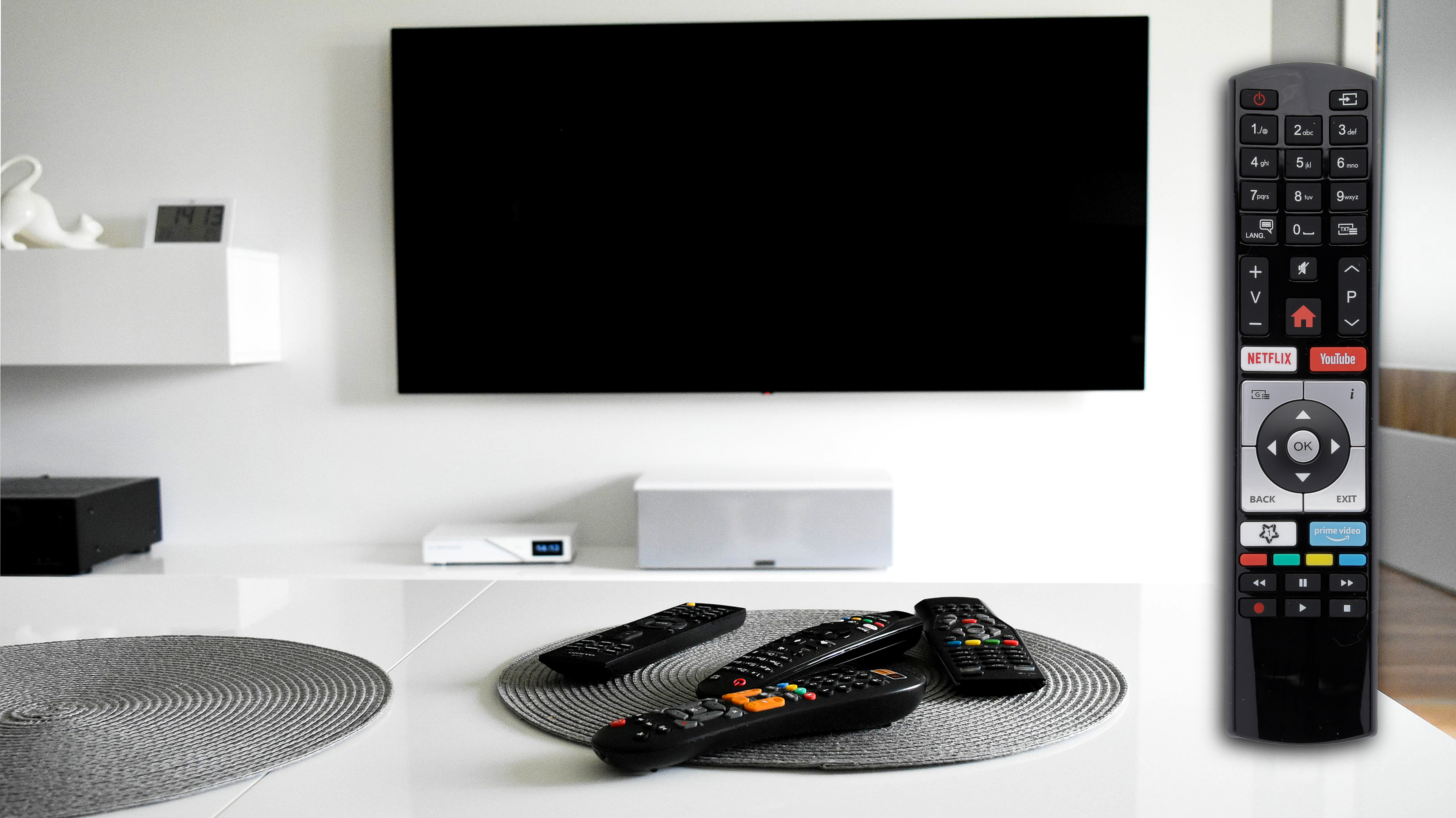 Fernseher, Fernbedienungen auf einem Tisch, weißer Lautsprecher, Digitaluhr.