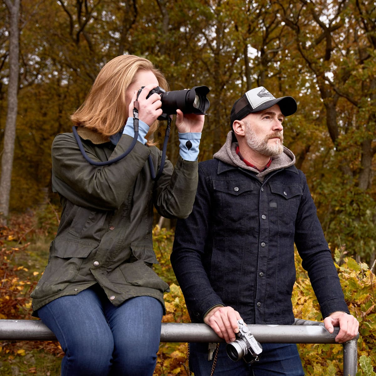 Eine Frau macht ein Foto, ein Mann schaut weg. Herbstbäume im Hintergrund.