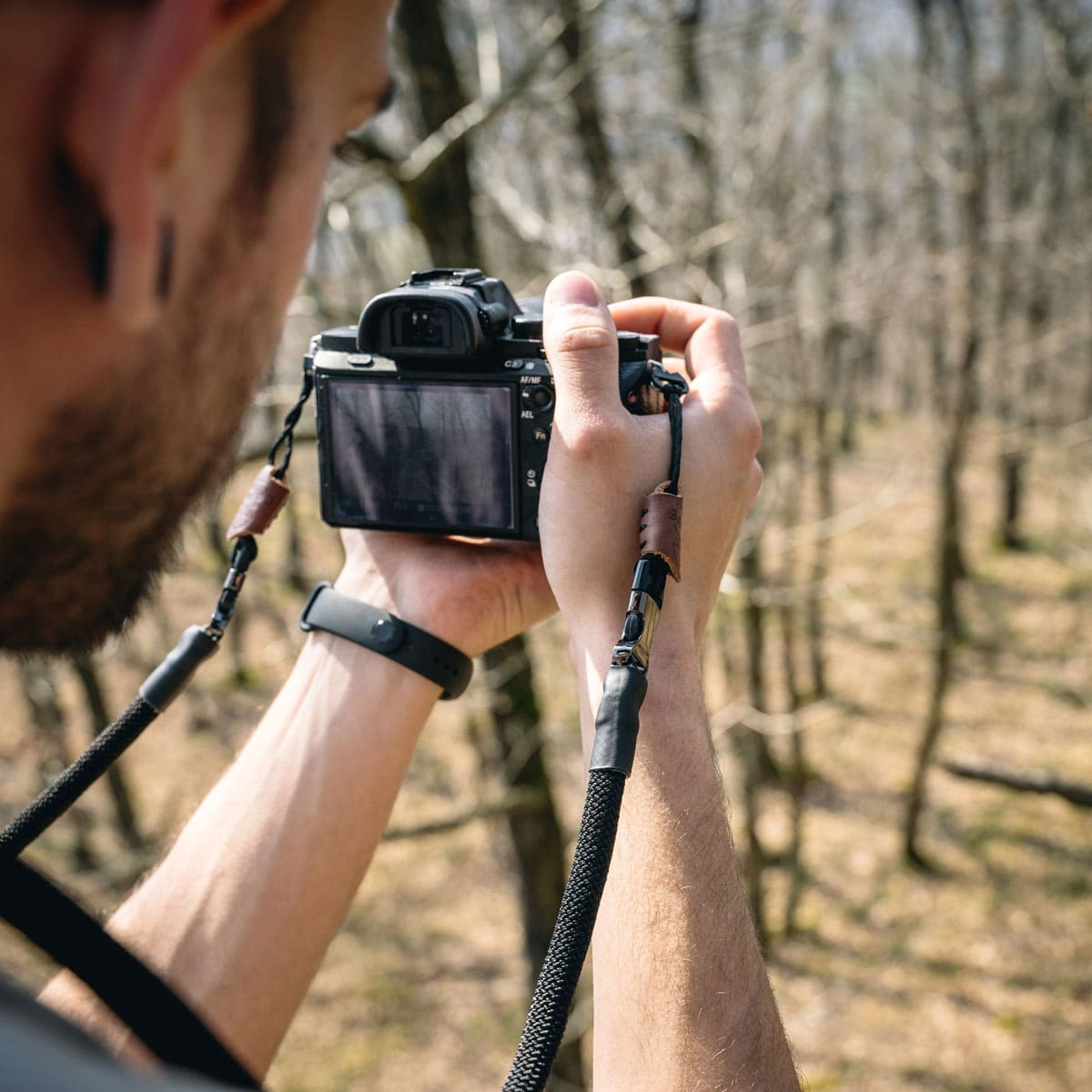 Person hält Kamera in der Natur mit Gurt. Waldhintergrund.