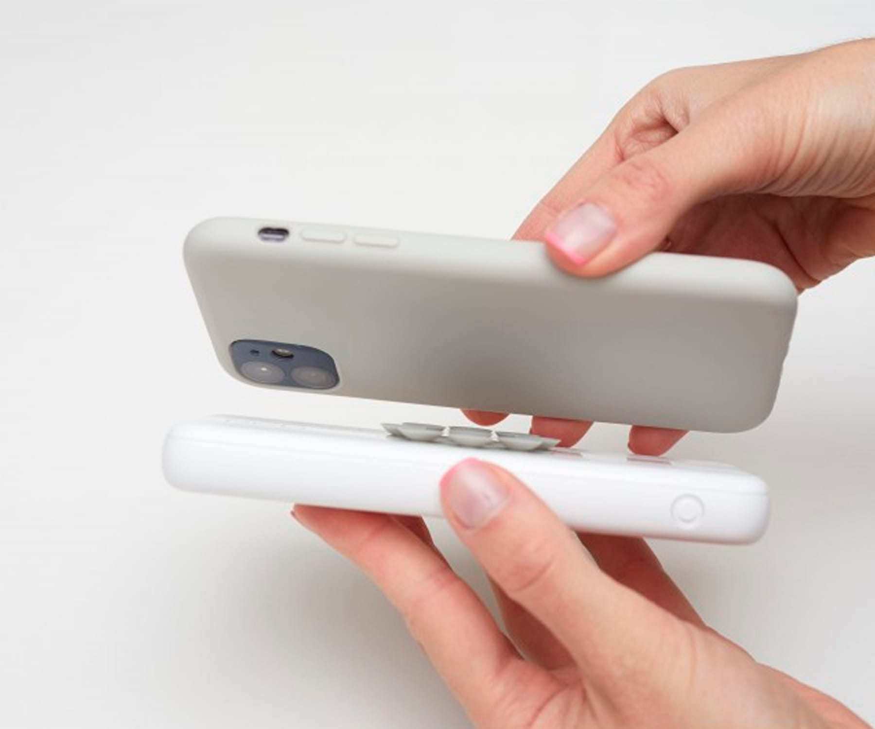 Manos sosteniendo un teléfono y un cargador blanco, el teléfono en una funda gris está encima del cargador.