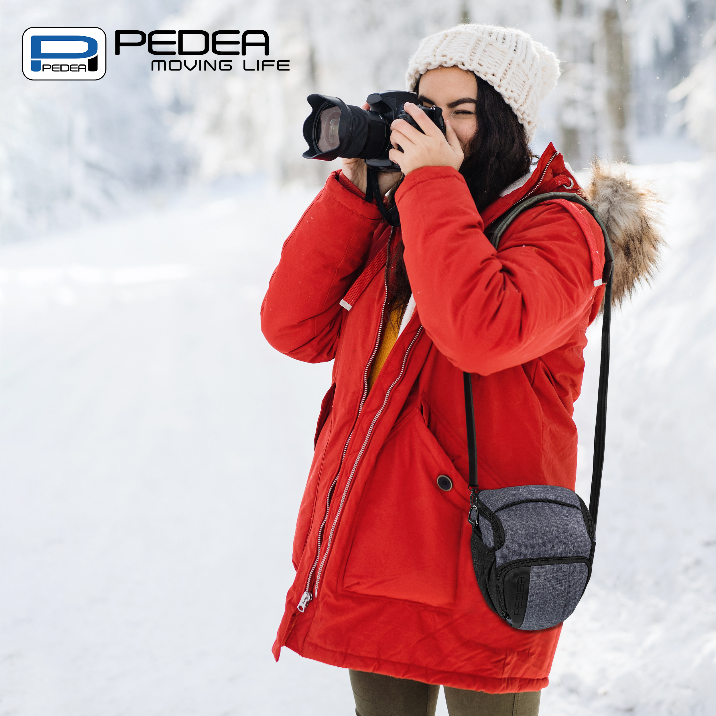 Frau in roter Jacke fotografiert mit Kamera in verschneiter Umgebung. Kameratasche sichtbar.