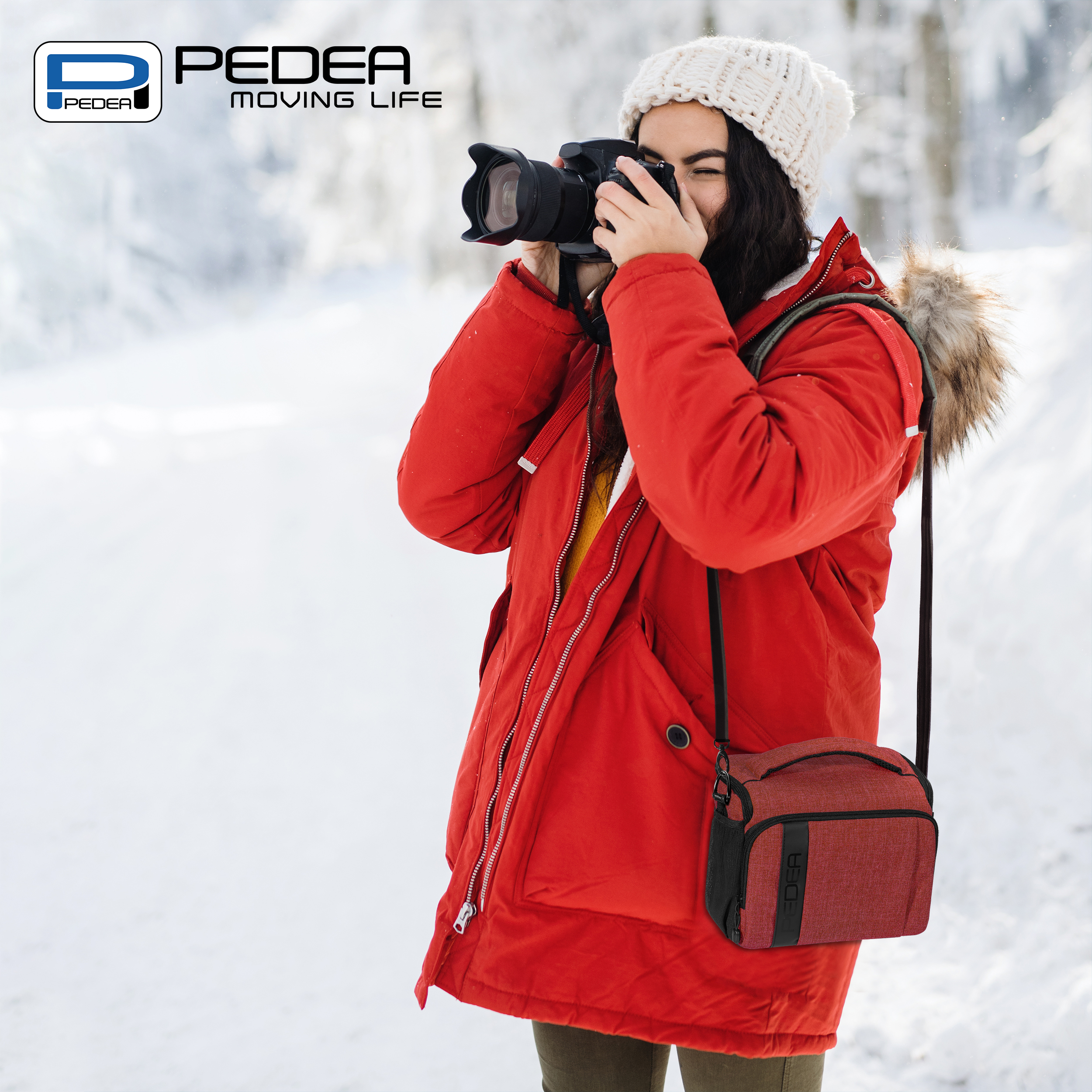 Eine Frau in rotem Mantel fotografiert mit einer Kamera. Sie hält eine Kameratasche in verschneiter Umgebung.
