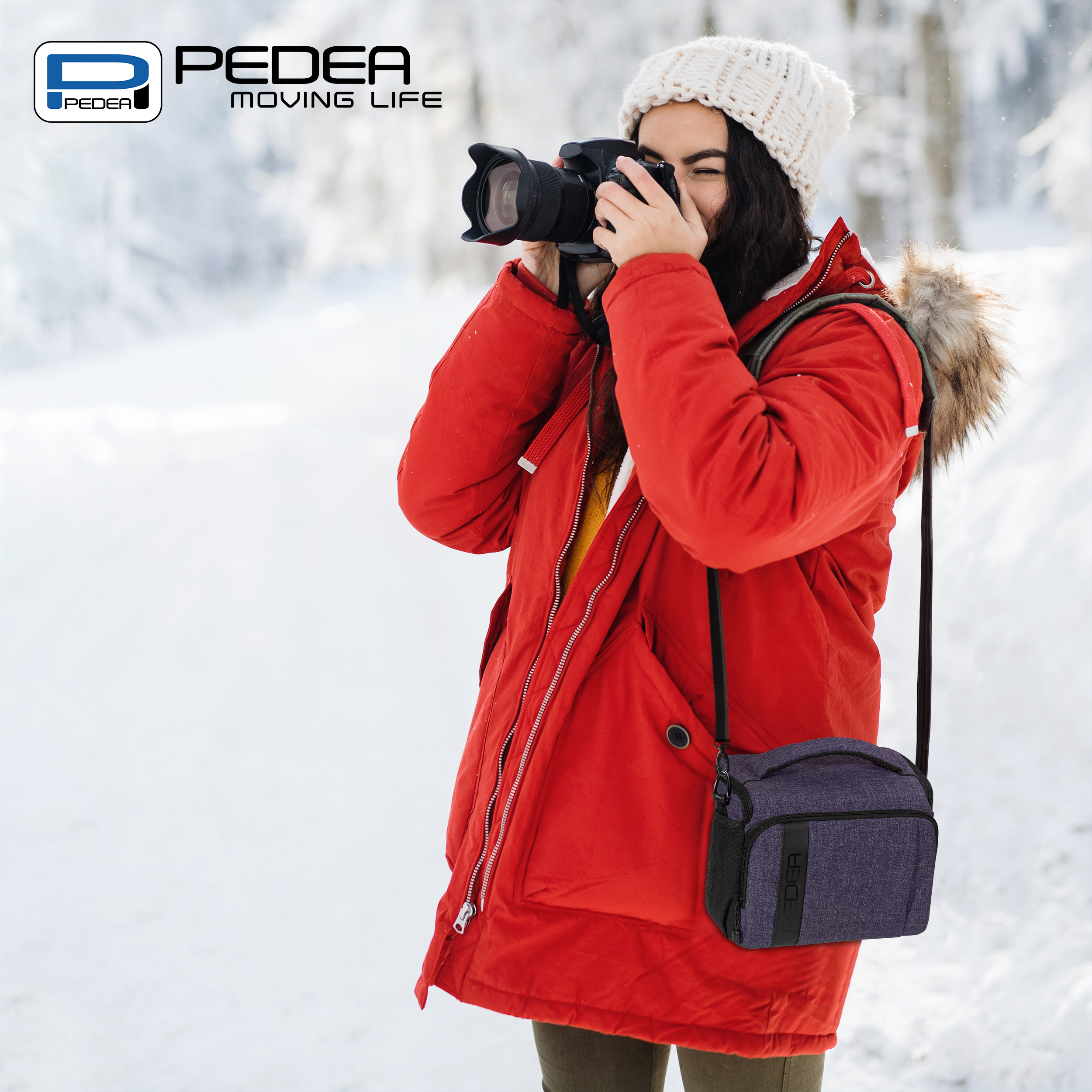 Eine Frau in rotem Mantel und weißem Hut fotografiert im Schnee. Sie hat eine Kameratasche.