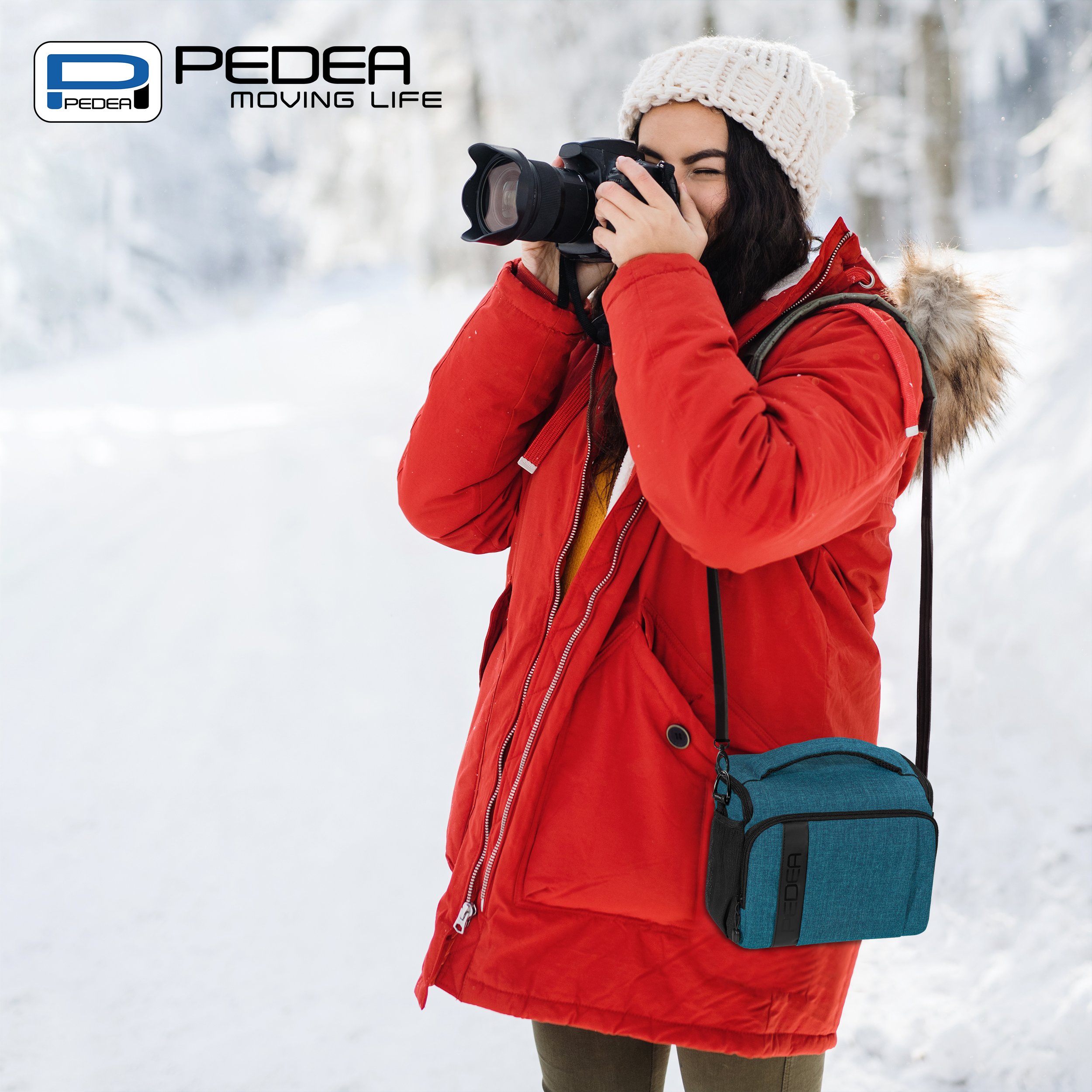 Eine Frau macht ein Foto in einem verschneiten Wald, trägt eine rote Jacke und eine teal-farbene Kameratasche.