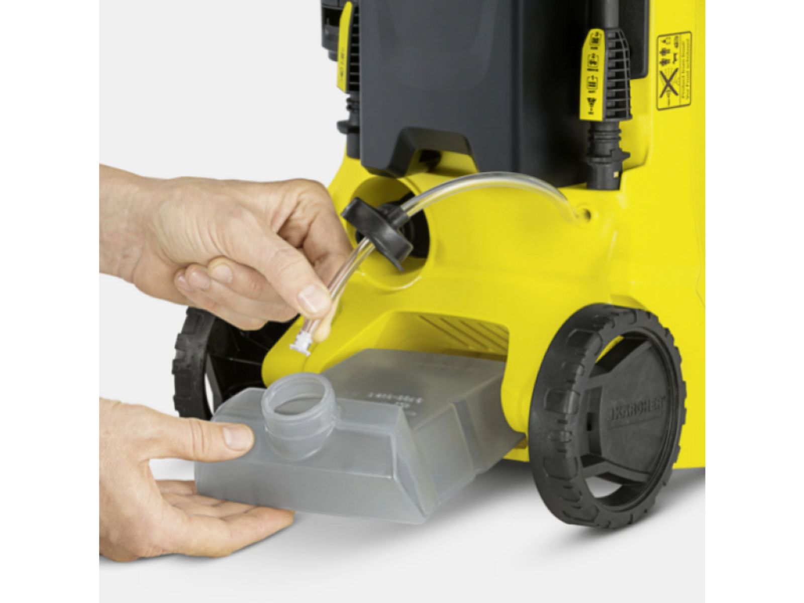 Osoba podłącza rurę do żółtej myjki ciśnieniowej. Przezroczysty pojemnik na pierwszym planie.