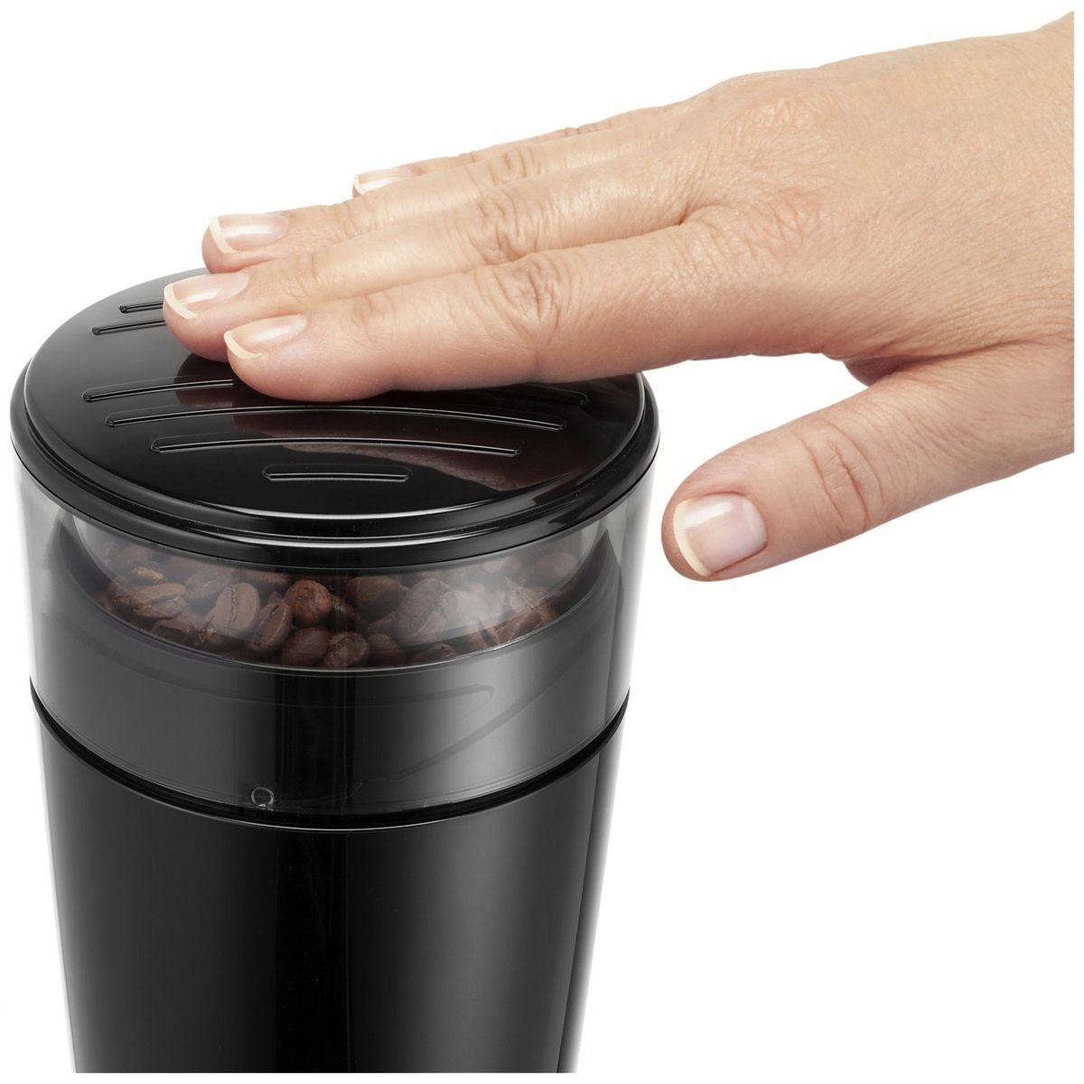Dłoń nad czarnym młynkiem do kawy z widocznymi ziarnami kawy.