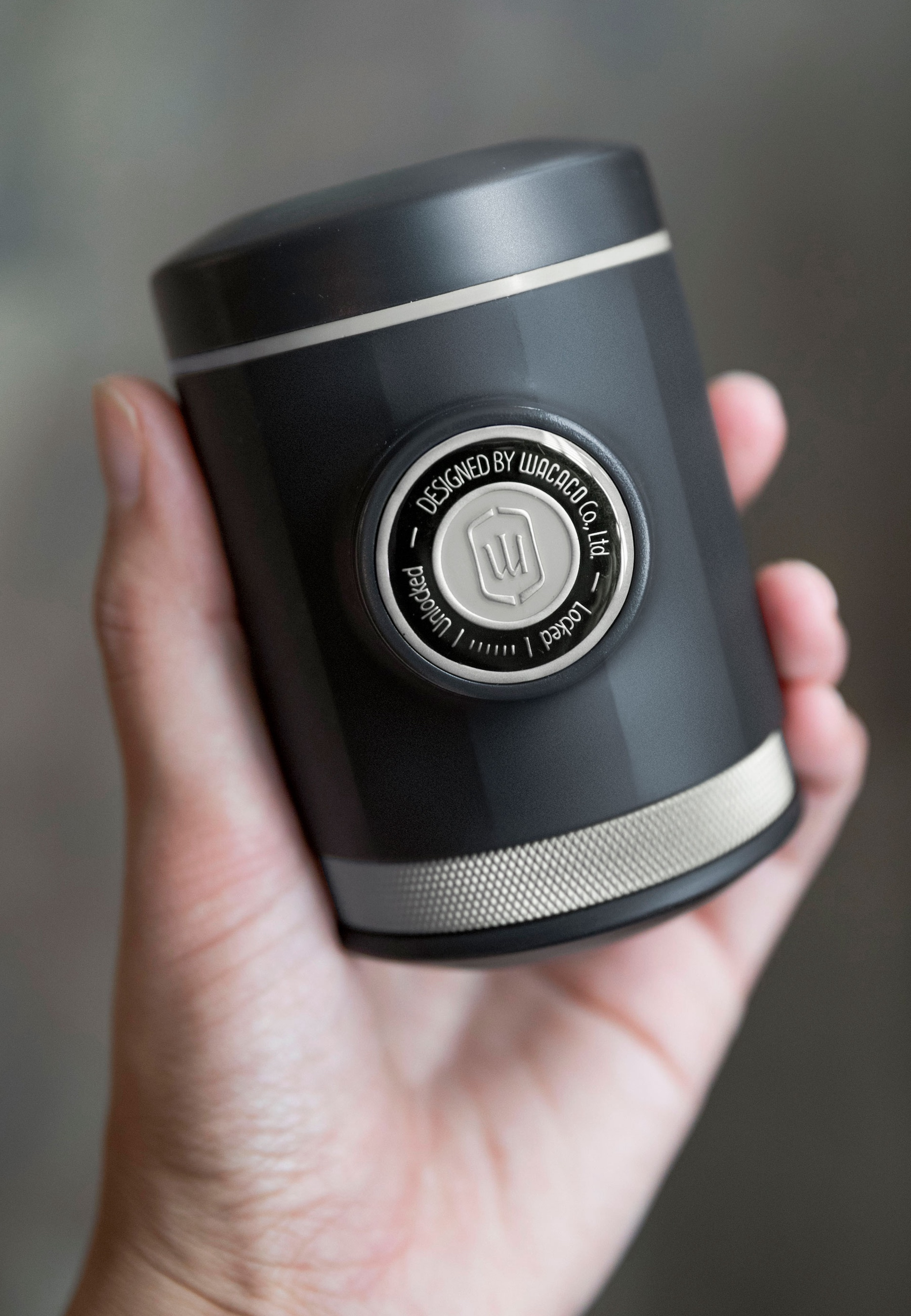 Mano che tiene una macchina per espresso portatile nera. Bordo argentato e un'etichetta.