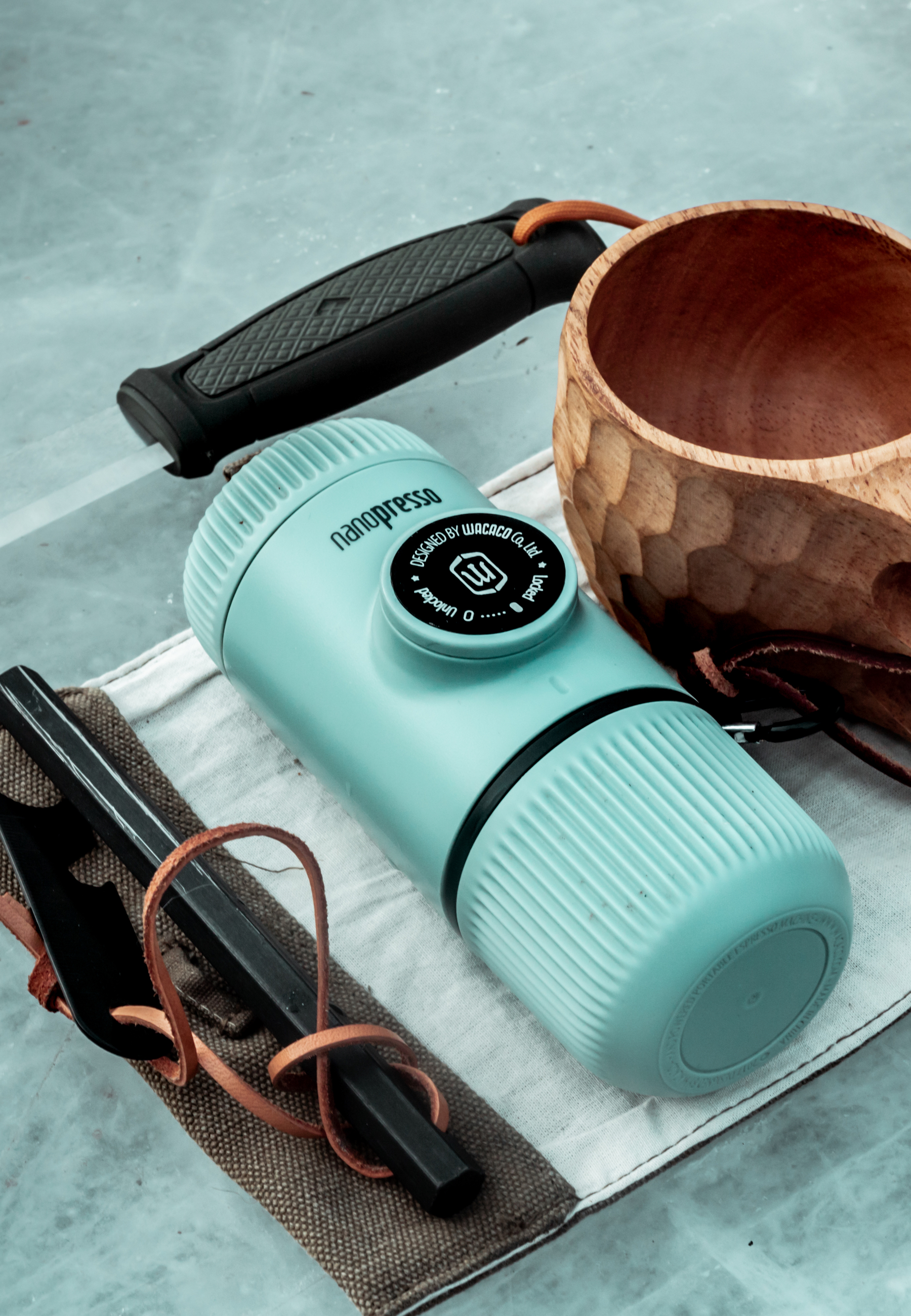 Tragbarer Espressomaker, mintgrün, mit Holzbecher und Messer. Auf heller Oberfläche.