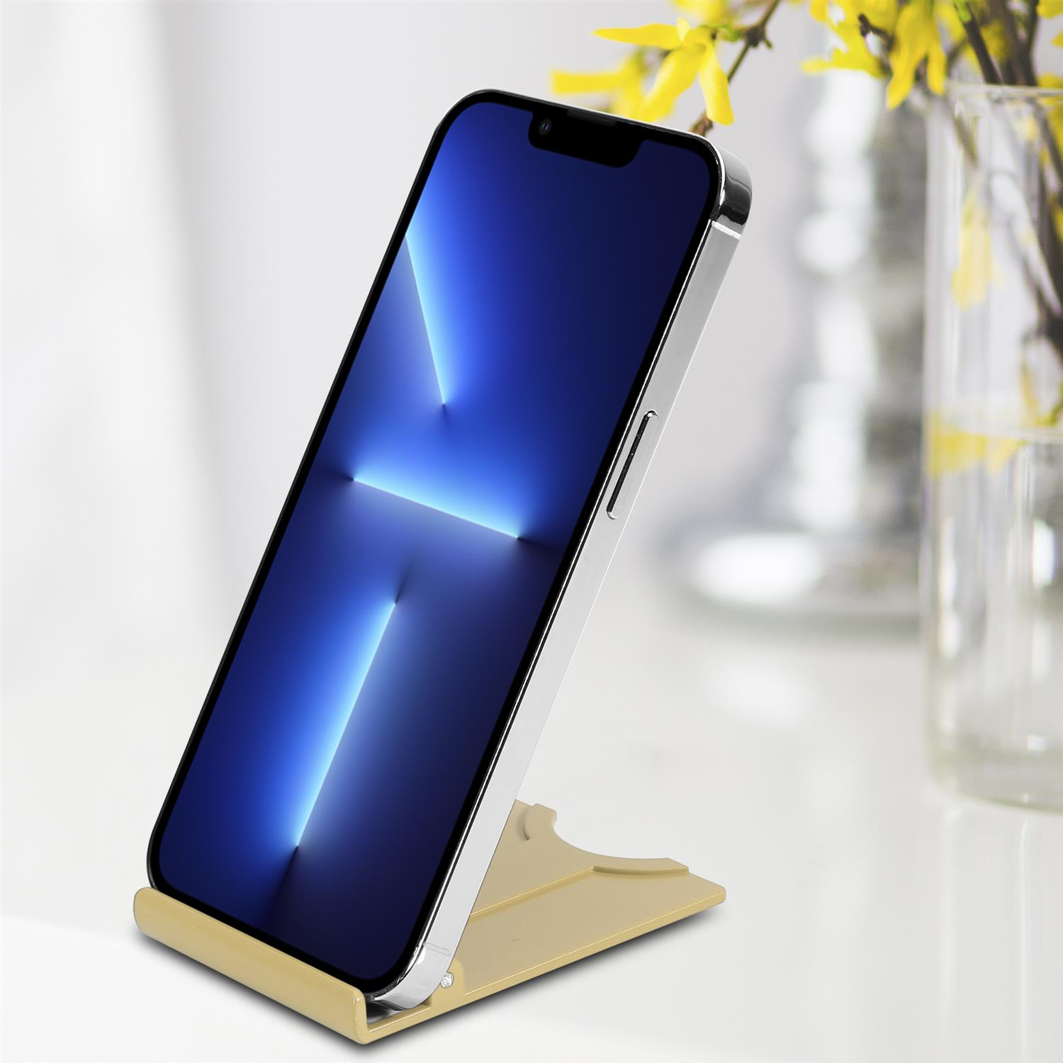 Ein Smartphone auf einem beigen Ständer, gegen einen weißen Hintergrund, mit gelben Blumen.