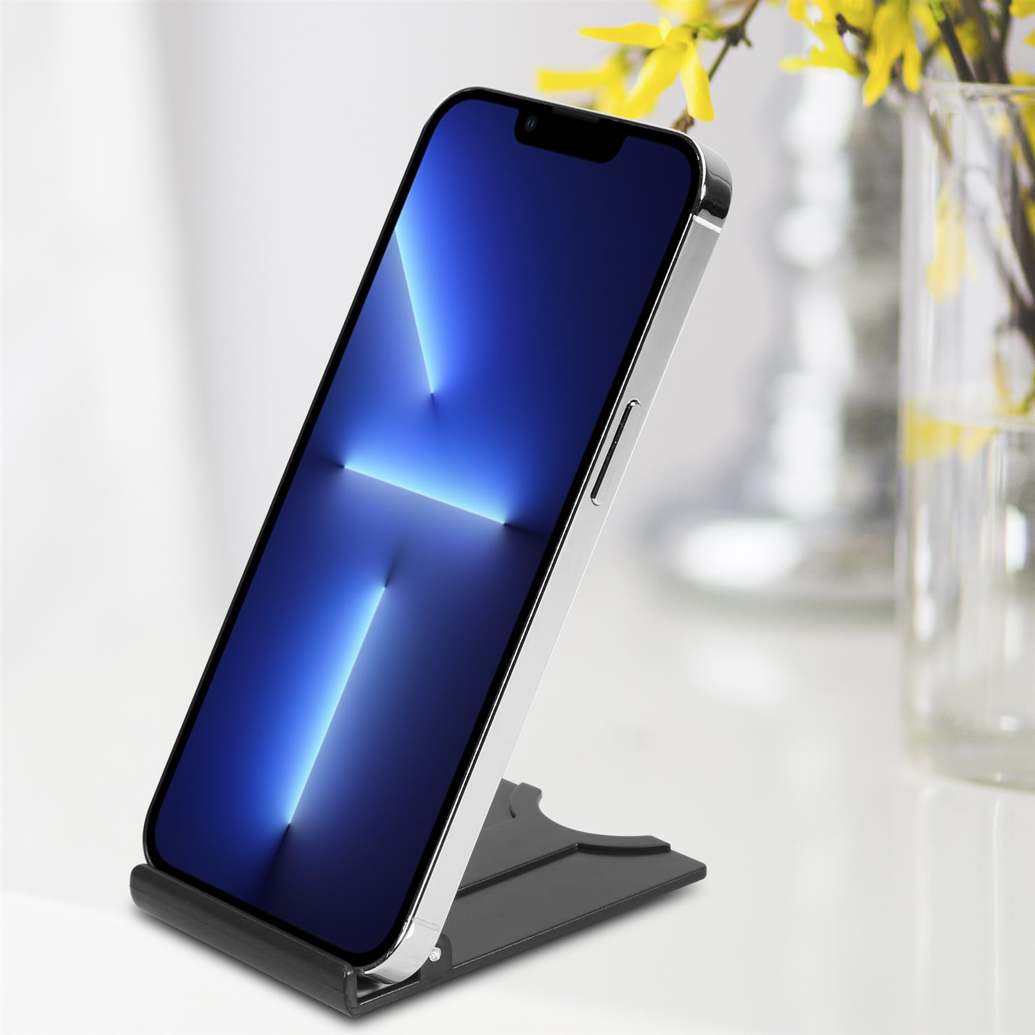 Silbernes Telefon auf einem schwarzen Ständer. Hintergrund: Tisch, Blumen in einer Vase, verschwommener Hintergrund.