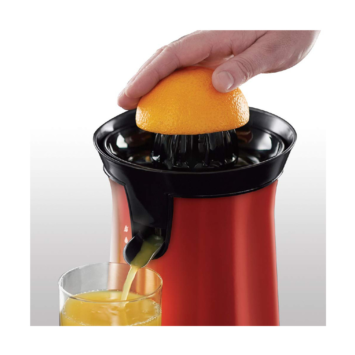 Eine Person, die eine Orange in einen rot-schwarzen elektrischen Entsafter mit einem klaren Glas auspresst.