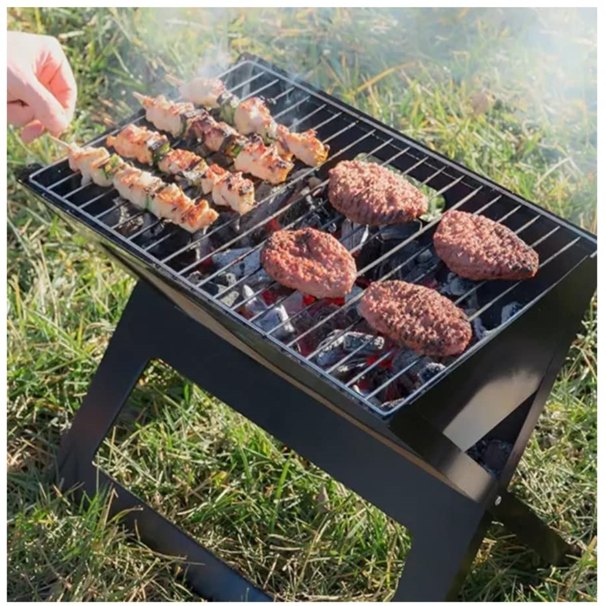 Ein tragbarer schwarzer Grill mit Spießen und Burgern, die über glühenden Kohlen braten.