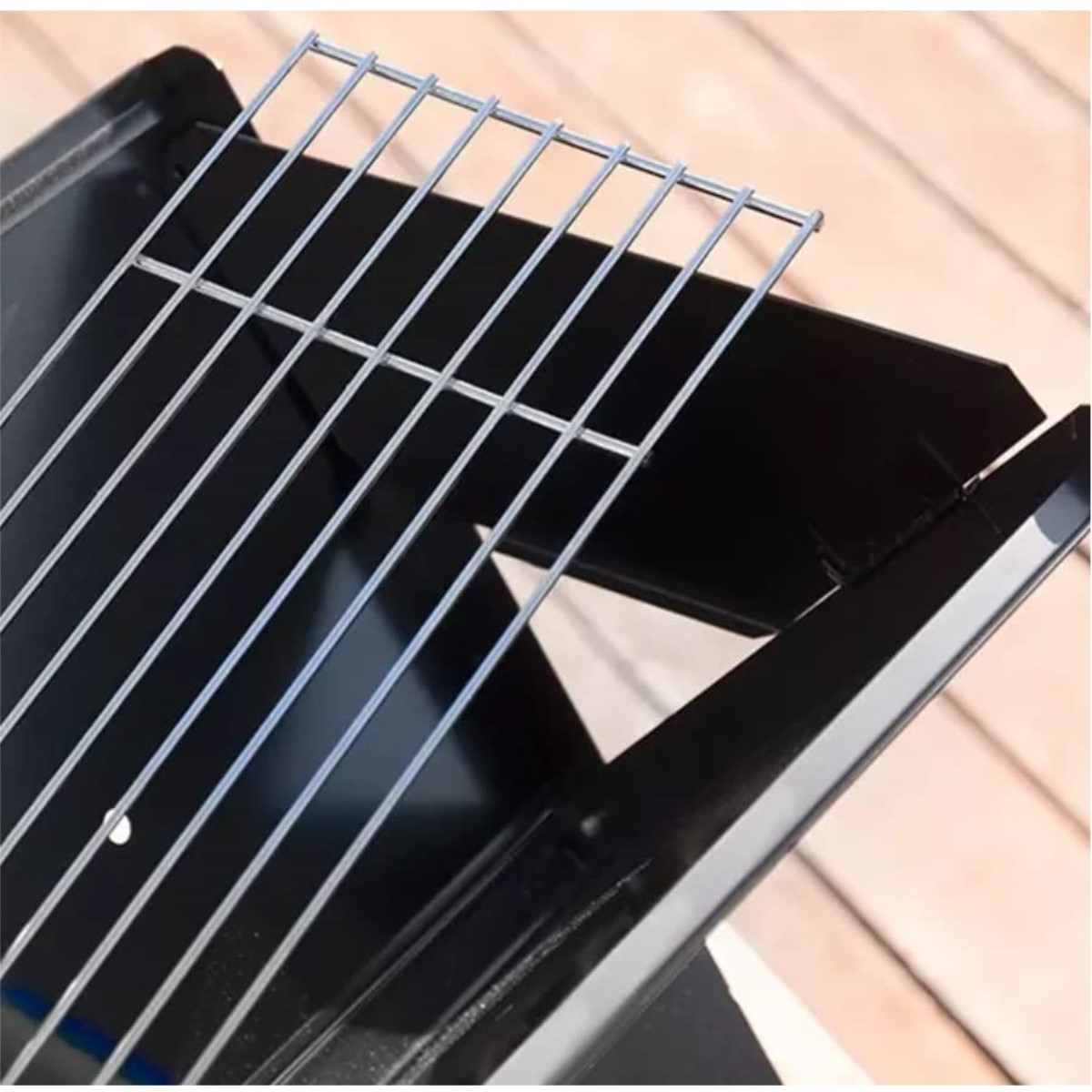 Nahaufnahme eines schwarzen Grills mit silbernen Stäben auf schwarzem Rahmen, über Holz.