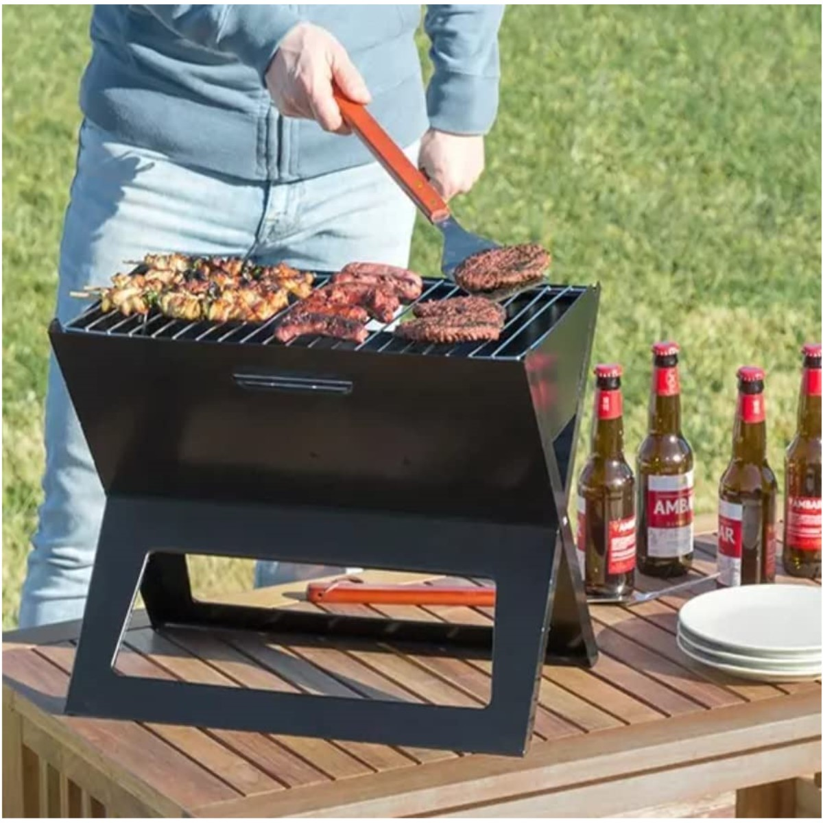 Eine Person grillt Essen auf einem tragbaren schwarzen Grill auf einem Holztisch im Freien.