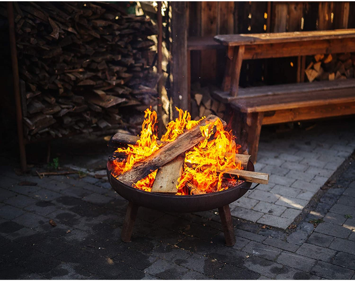 Eine Feuerstelle mit brennendem Holz und Flammen. Holzbänke im Hintergrund.