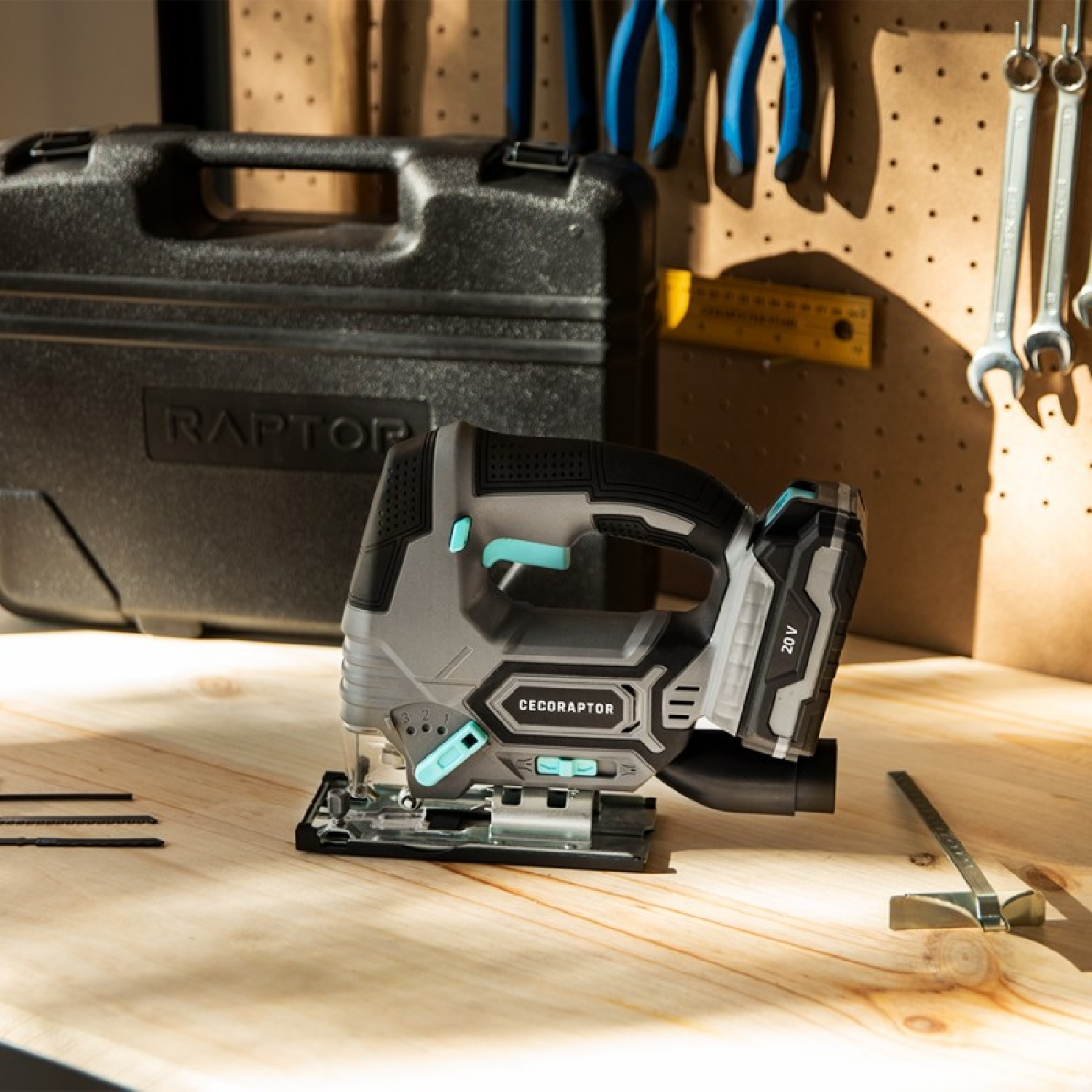 Szara bezprzewodowa wyrzynarka na drewnianym stole, czarna skrzynka narzędziowa i narzędzia na tablicy.