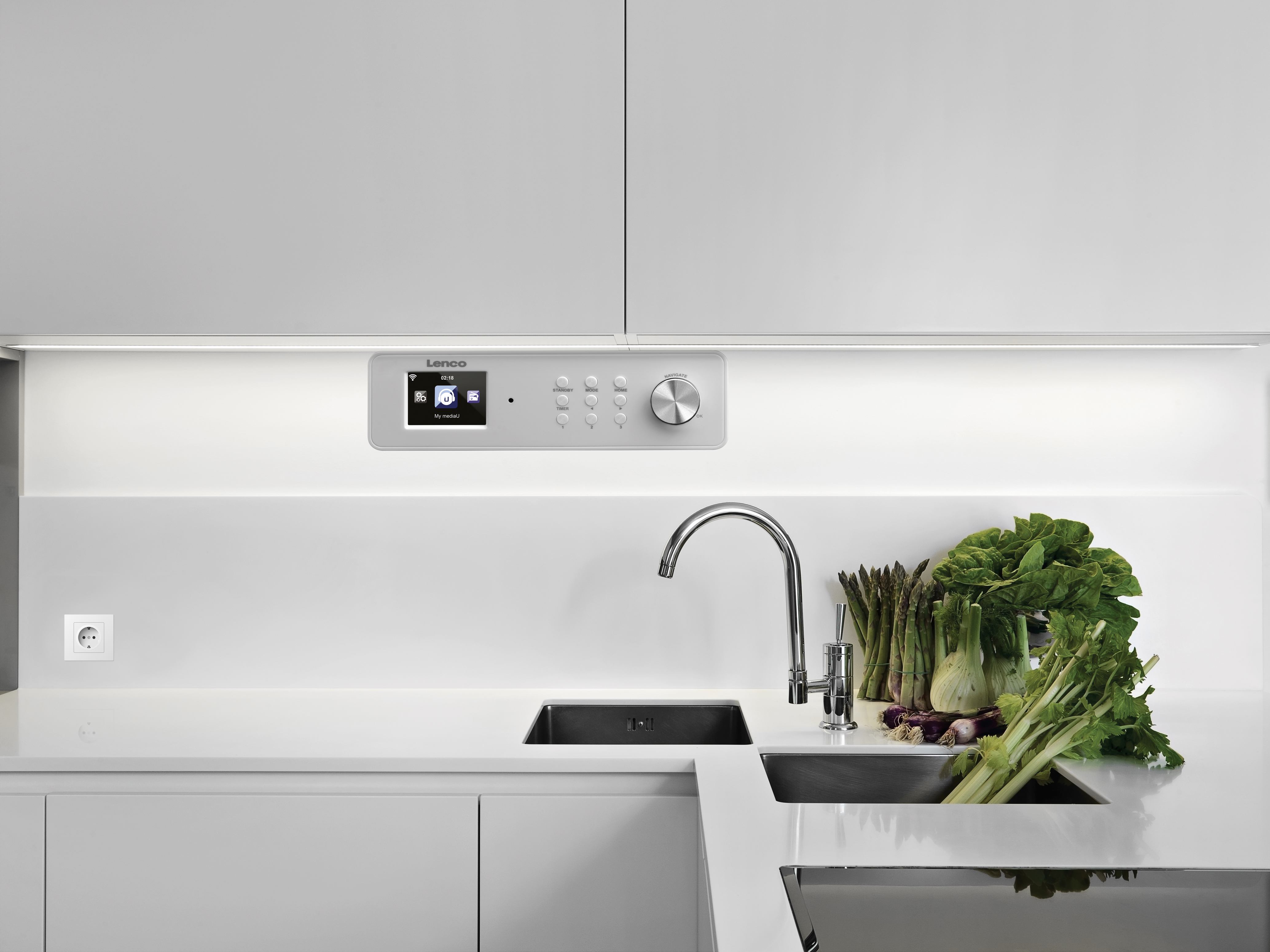 Kitchen scene with a radio control panel, sink, tap and vegetables on the counter.