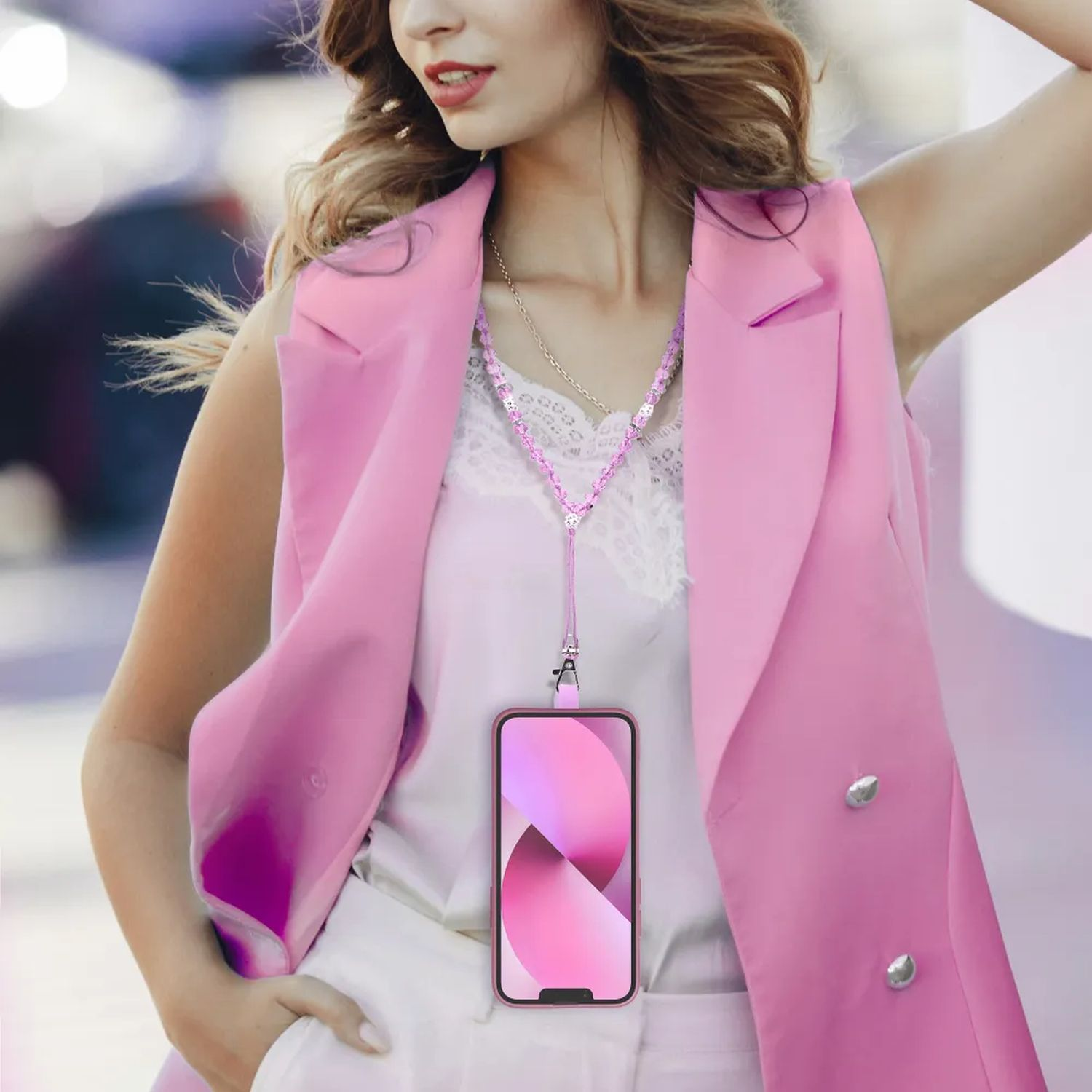 Frau mit pinker Weste hält Handy mit Lanyard. Weißes Shirt. Hintergrund unscharf.