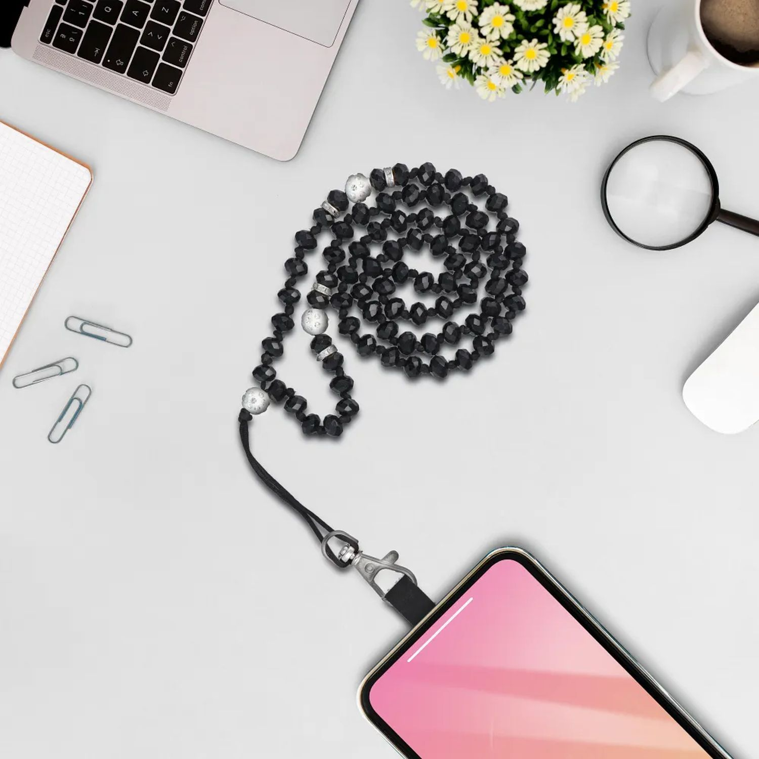 Eine Perlen-Telefon-Lanyard mit einem angeschlossenen Telefon. Ein Laptop, eine Maus und Zubehör liegen auf dem Tisch.