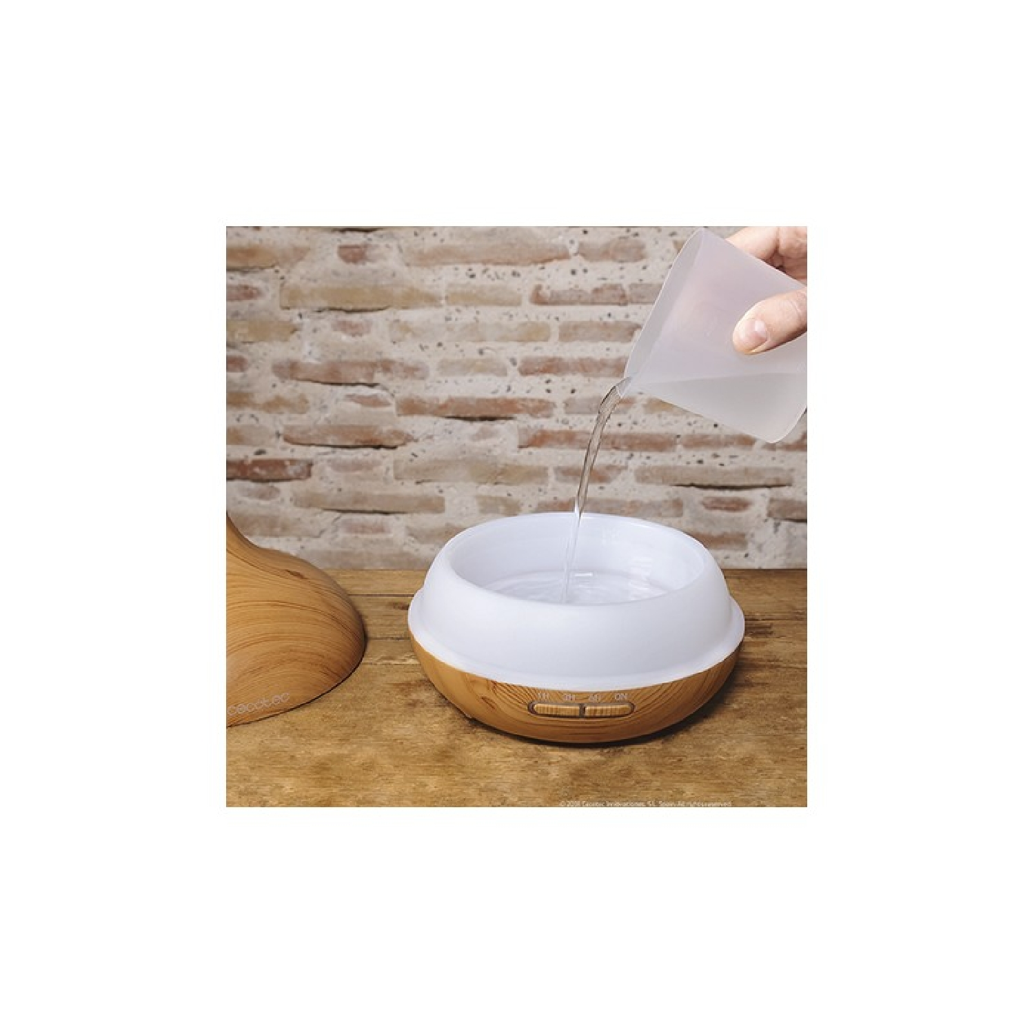 Una persona versa acqua in un diffusore per aromaterapia in legno e bianco.