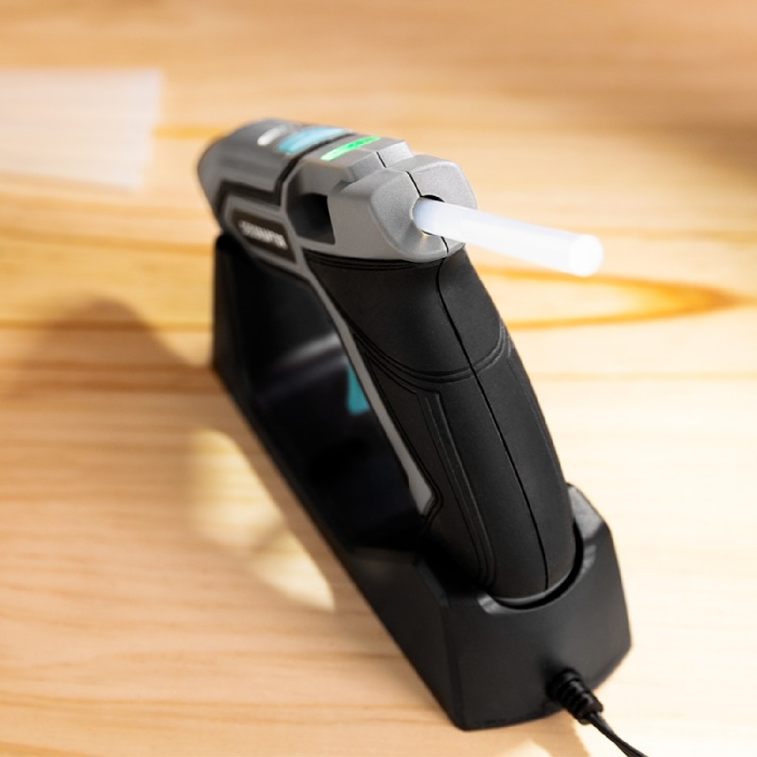 Szaro-czarny pistolet do kleju z białą sztyftem kleju, umieszczony na drewnianej powierzchni.