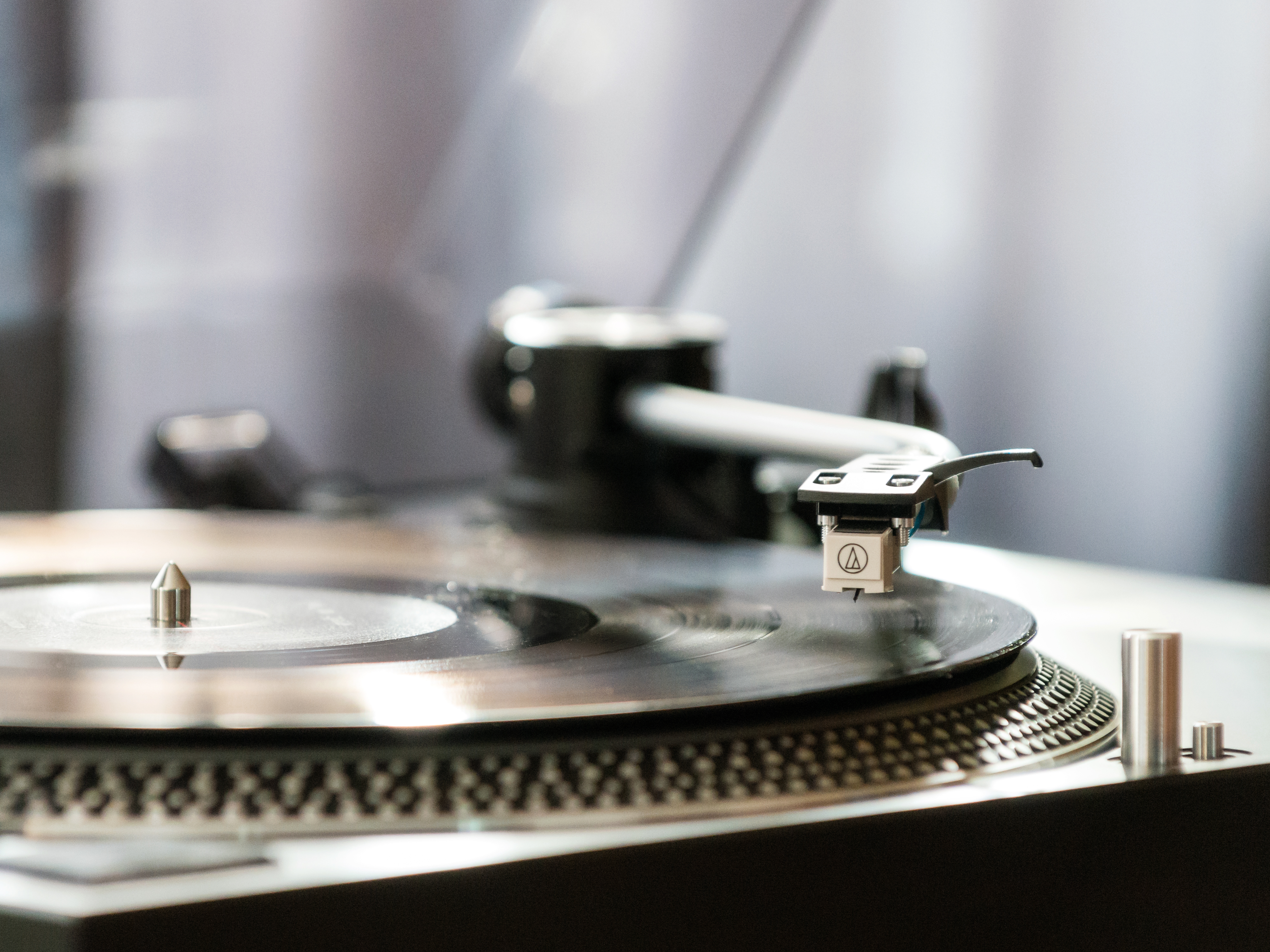 Gramofon z czarnym ramieniem i srebrną igłą odtwarzający czarną płytę winylową.