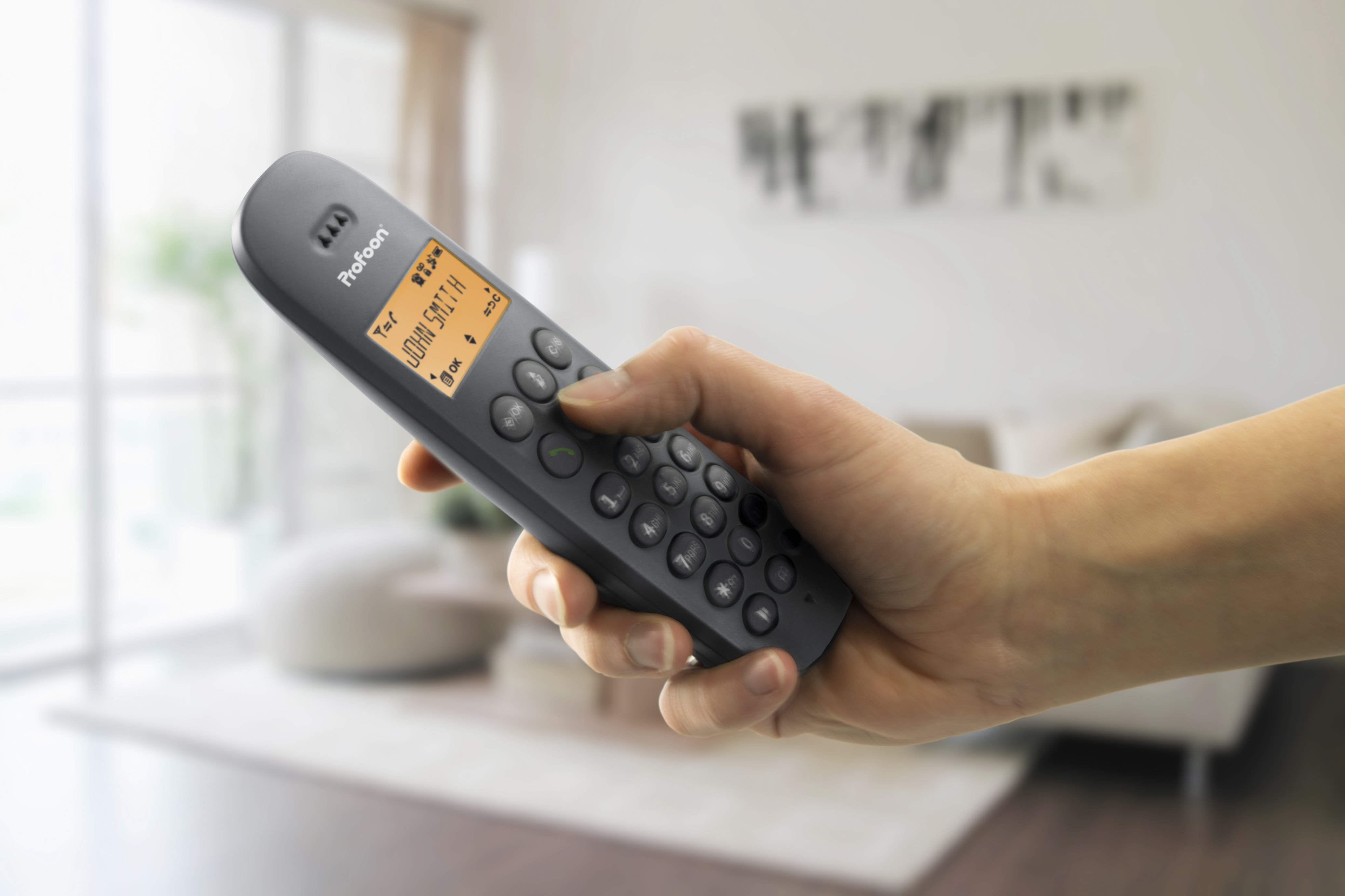 Hand hält graues schnurloses Telefon. Telefonbildschirm zeigt Namen und Nummer.