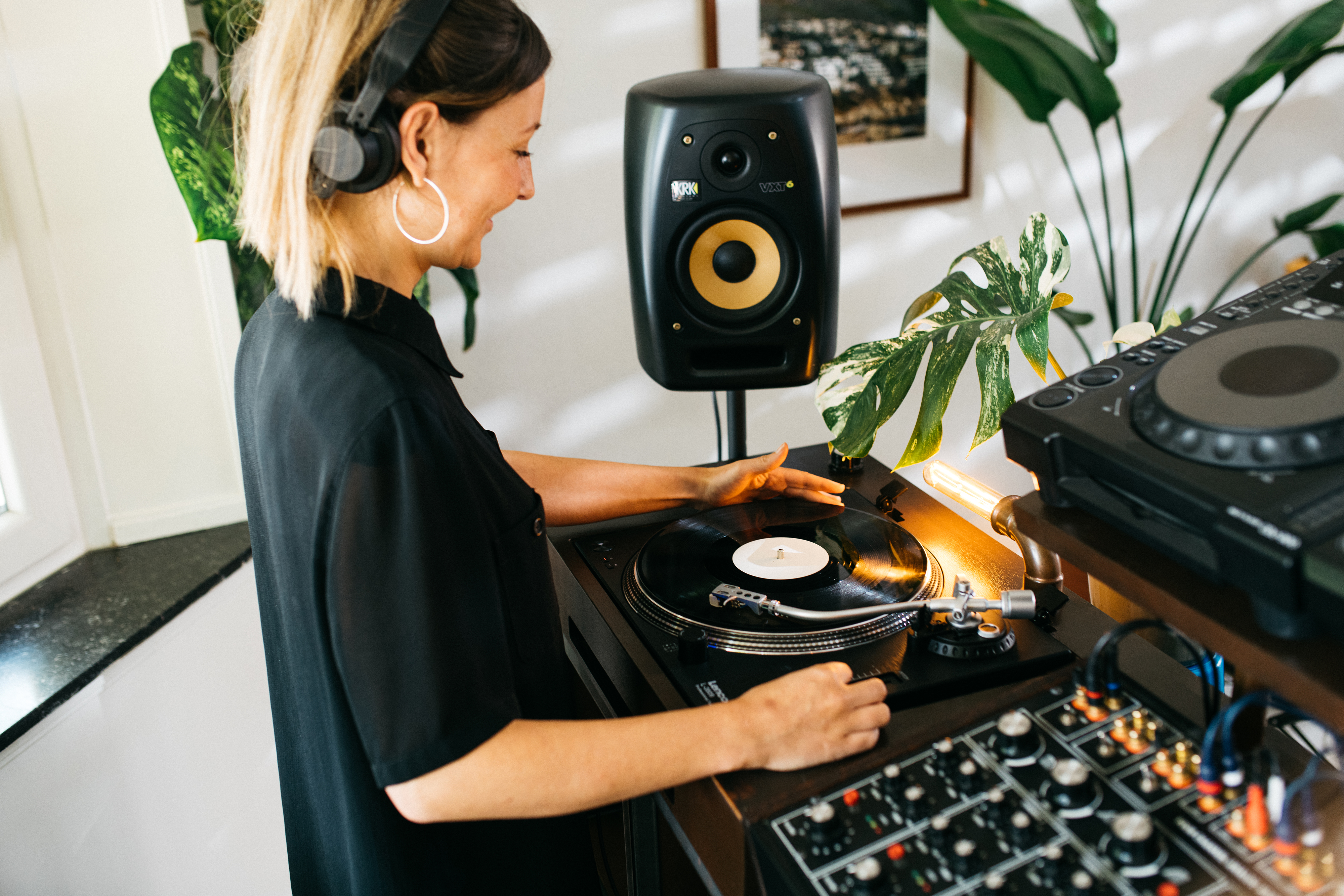 Eine DJ-Frau an einem Plattenspieler, die Musik mixt. Lautsprecher und Mischpult im Hintergrund.