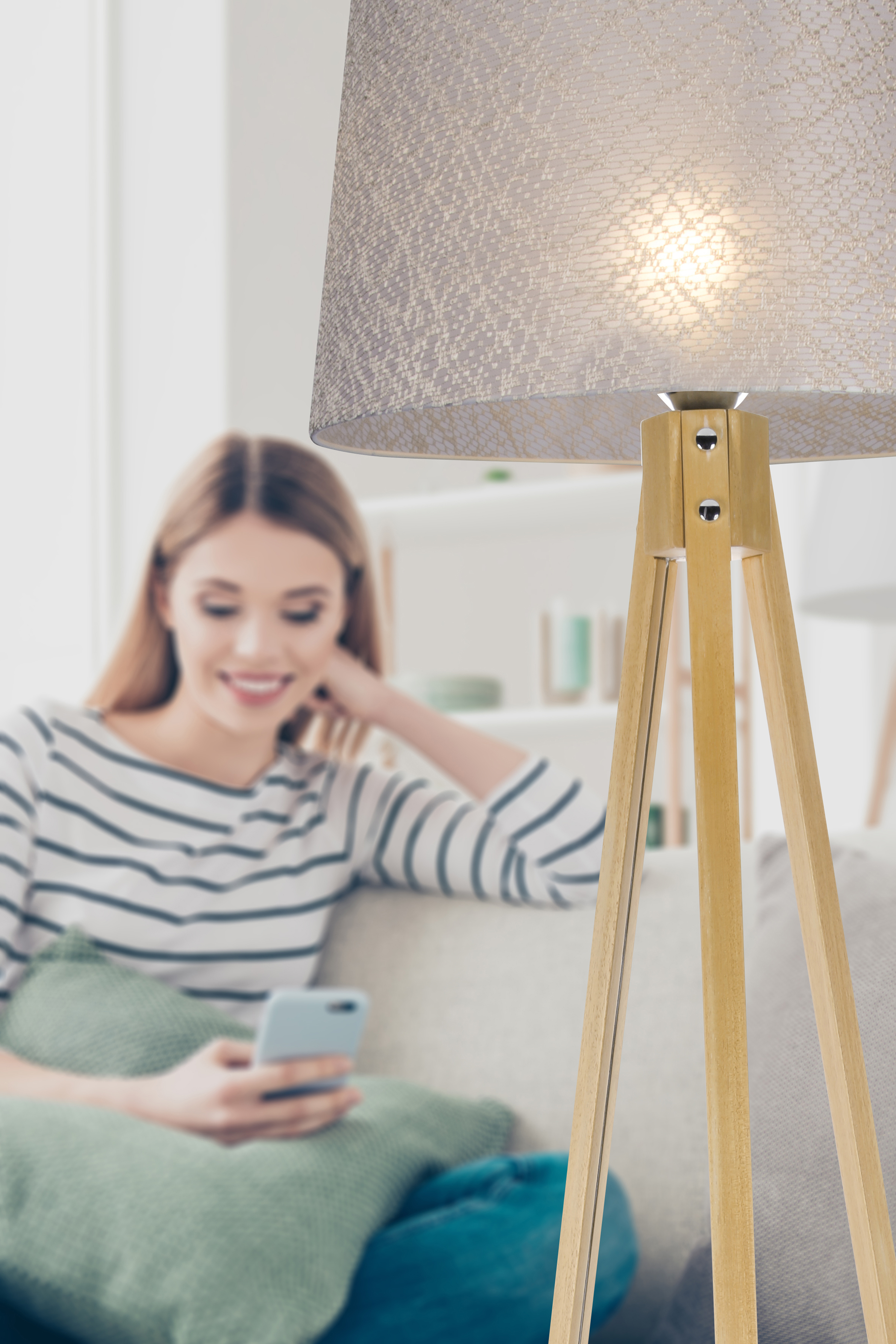 Eine Frau auf einem Sofa benutzt ein Telefon. Eine Stehlampe steht im Vordergrund mit einem Lampenschirm.