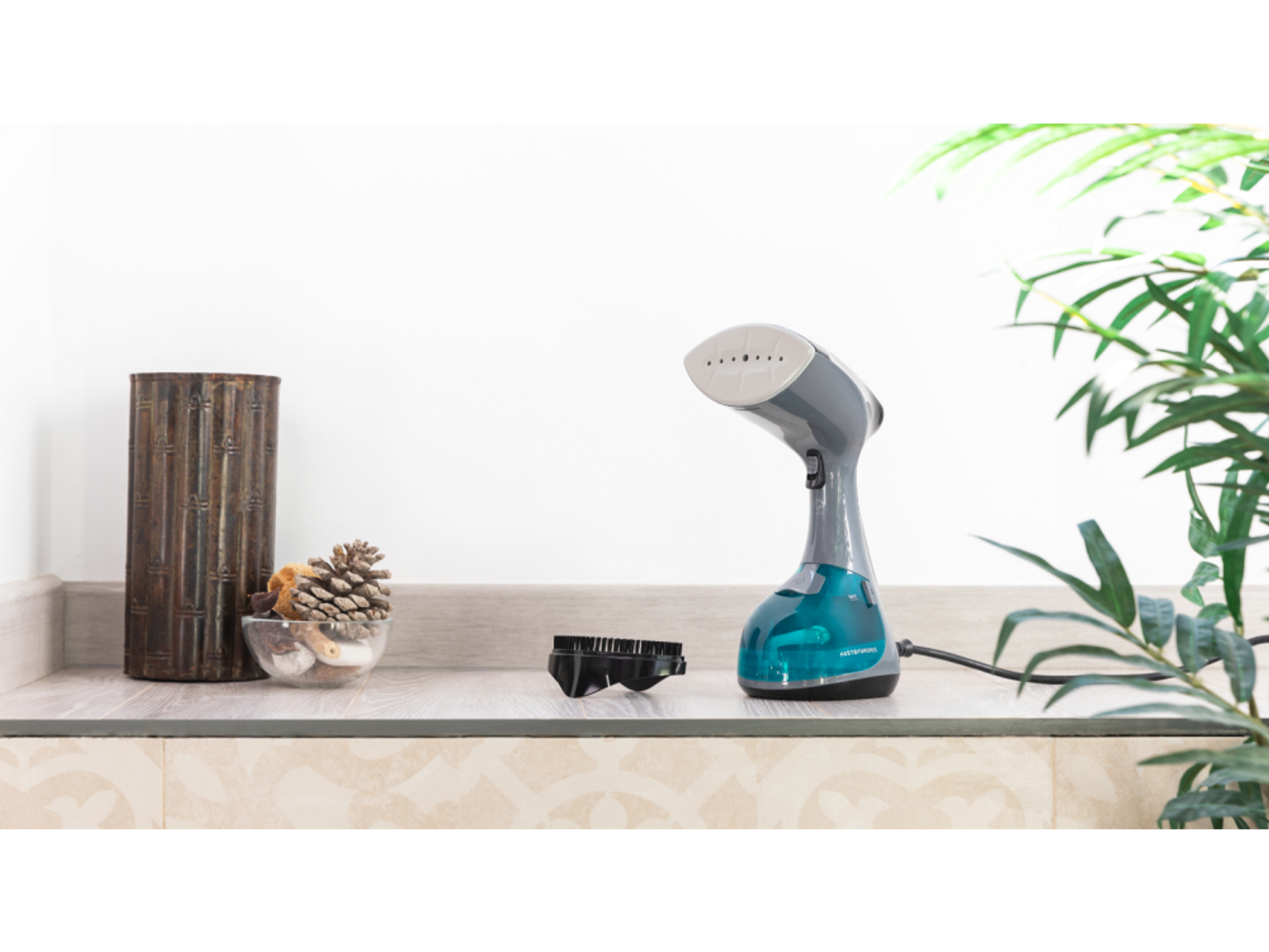 Żelazko parowe na blacie z akcesoriami. W tle wazon i rośliny.